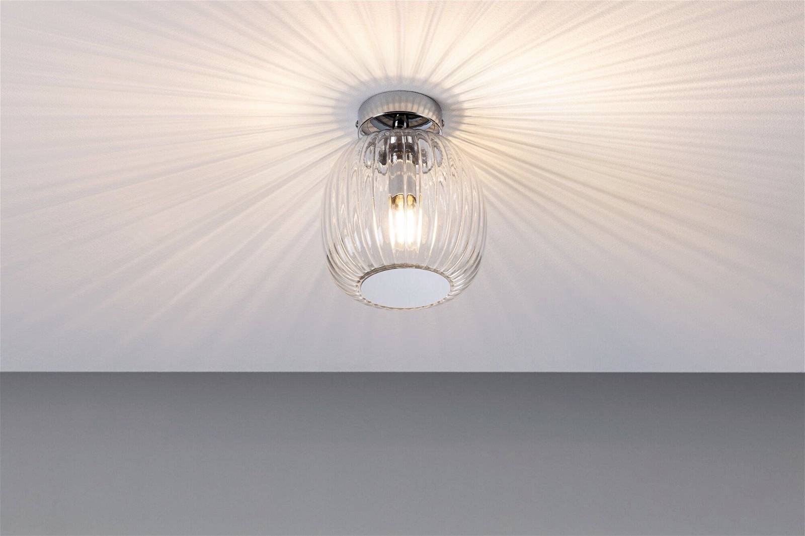 Lampa sufitowa z przezroczystym kloszem szklanym, która rzuca ciepłe światło o promieniowym wzorze na sufit.