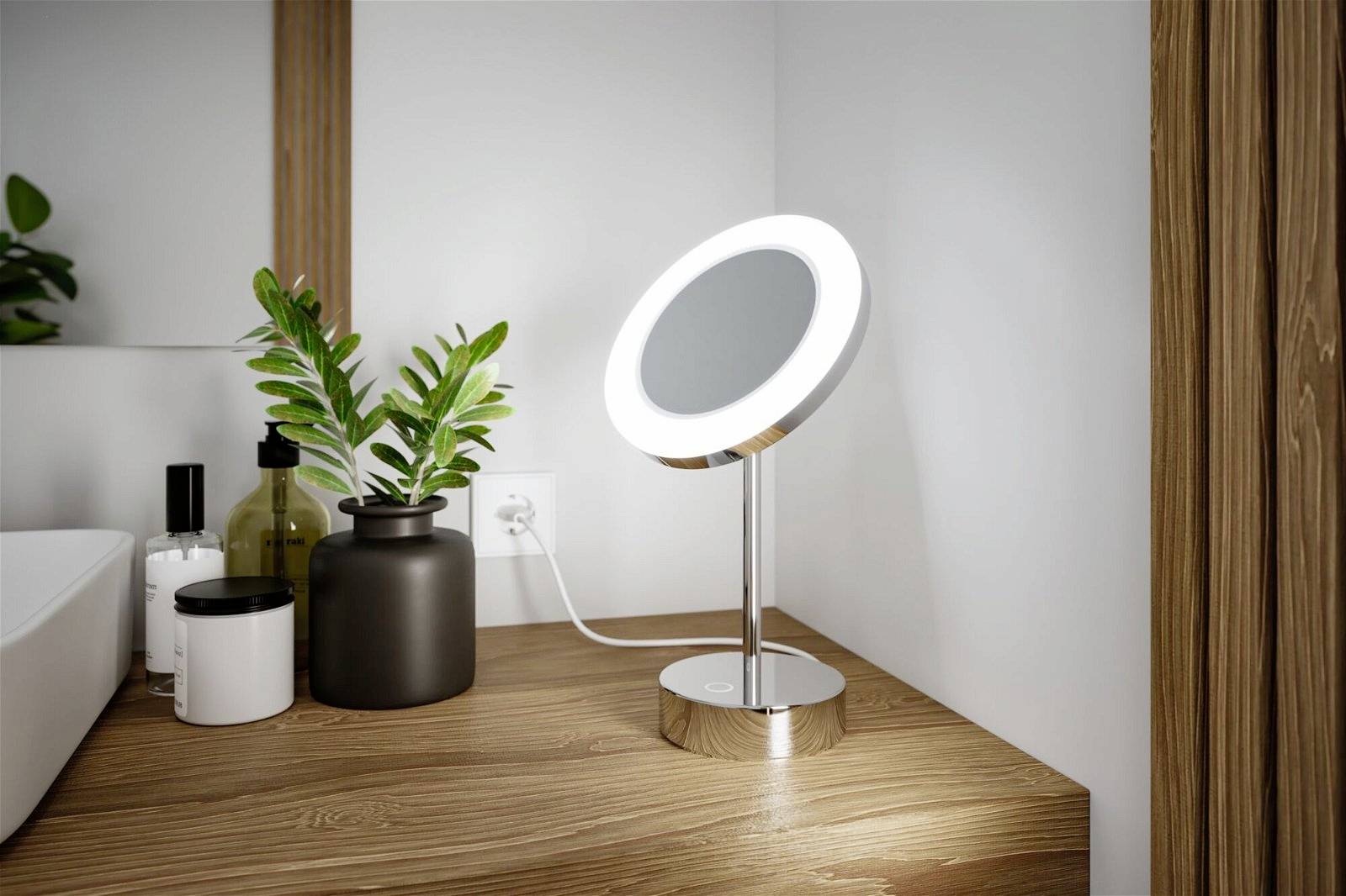 Podświetlone lustro kosmetyczne stoi na drewnianym stole obok kosmetyków pielęgnacyjnych i zielonej rośliny w nowoczesnej łazience.