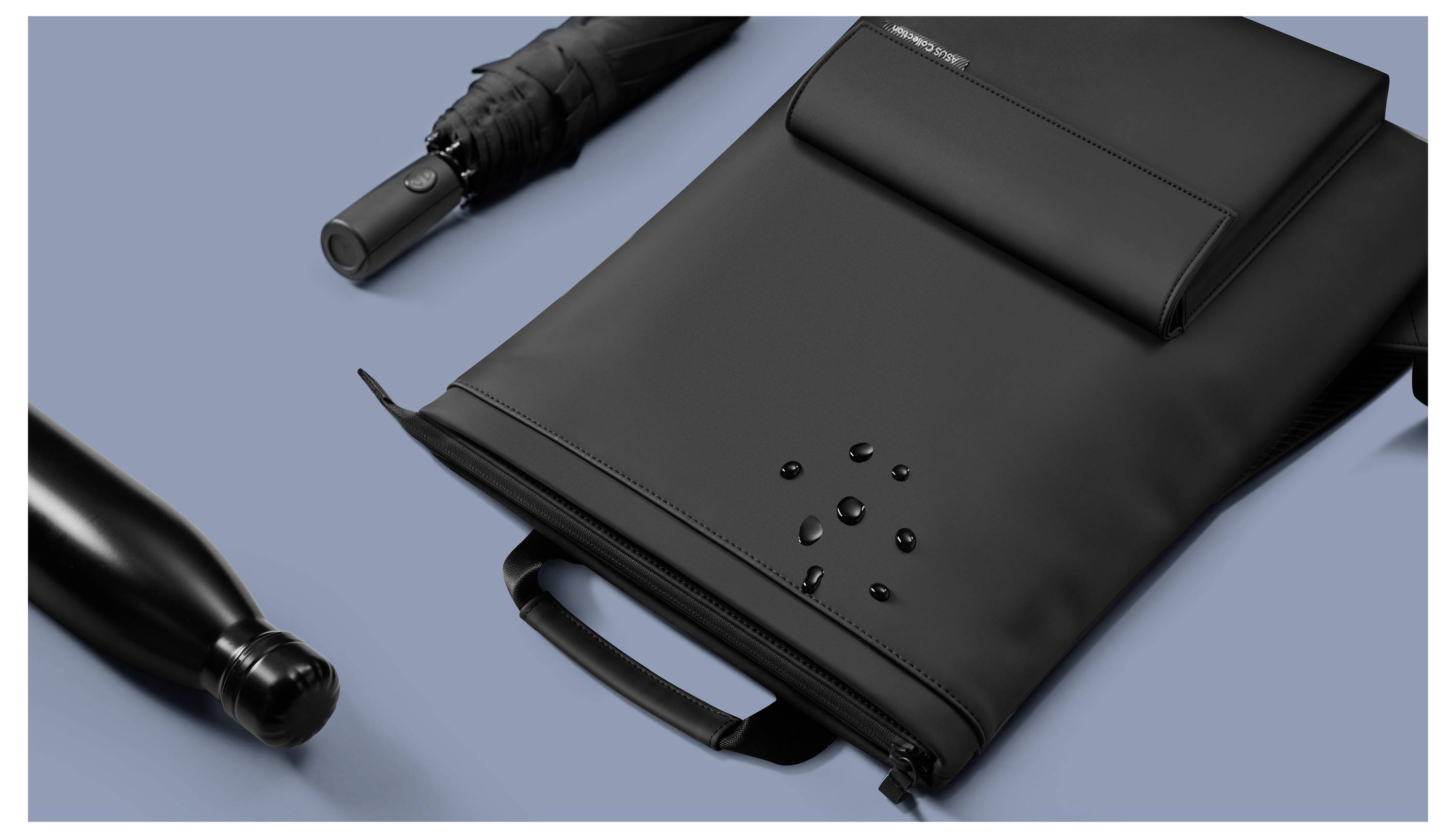 Szczupły, czarny plecak z technologią wodoodporną leży obok zwiniętej, czarnej butelki i parasola.