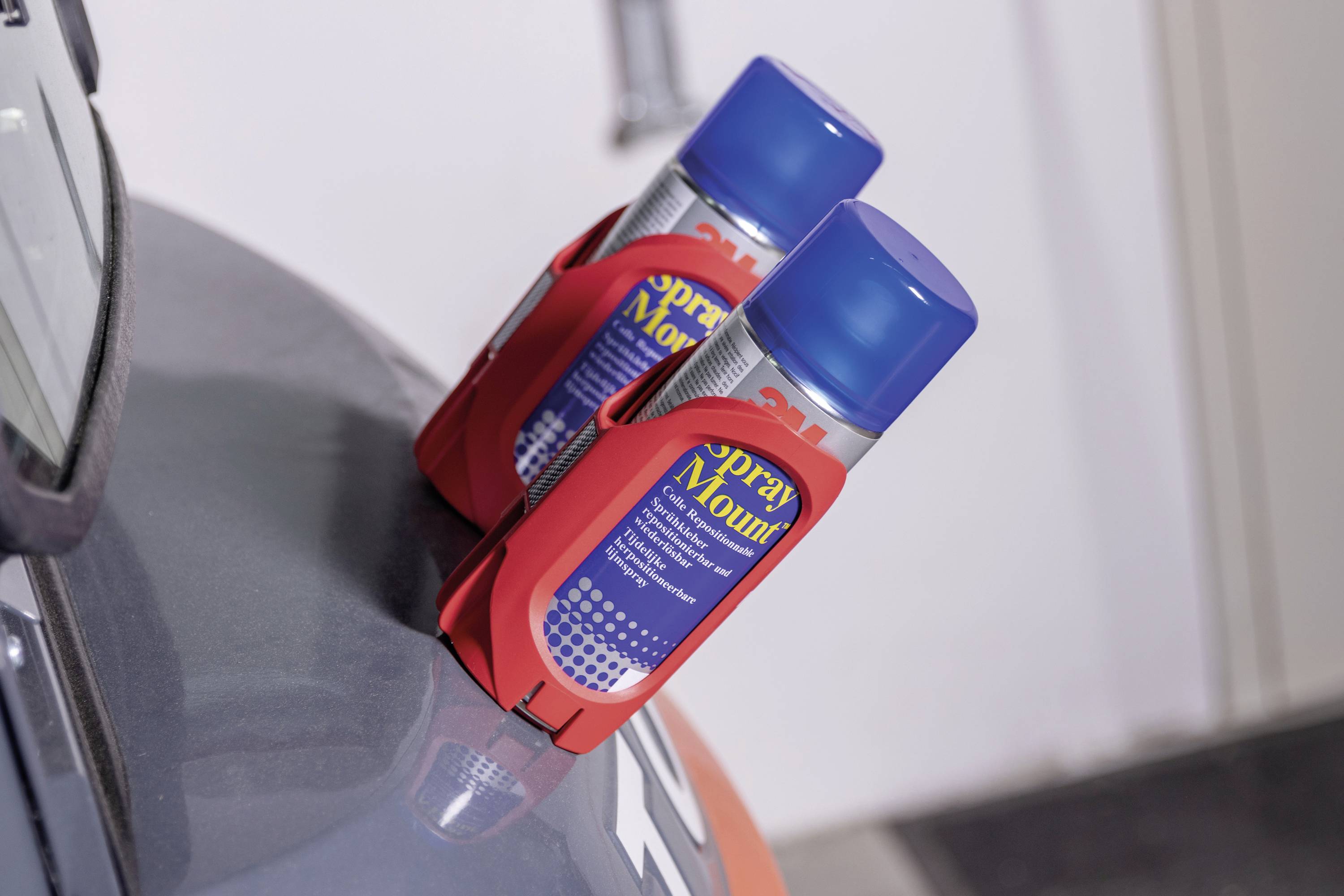 Dwie puszki z farbą w czerwonych uchwytach są umieszczone na krawędzi niebieskiego obiektu. Znajdują się wewnątrz pomieszczenia.