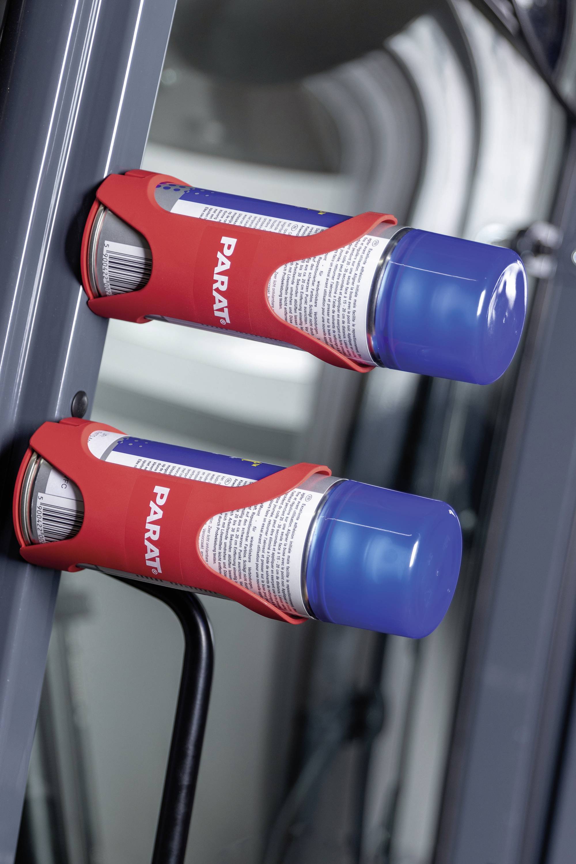 Dwa czerwone aparaty oddechowe Parat są zamontowane na ścianie i gotowe do użycia. Posiadają niebieskie nakładki i białe etykiety.