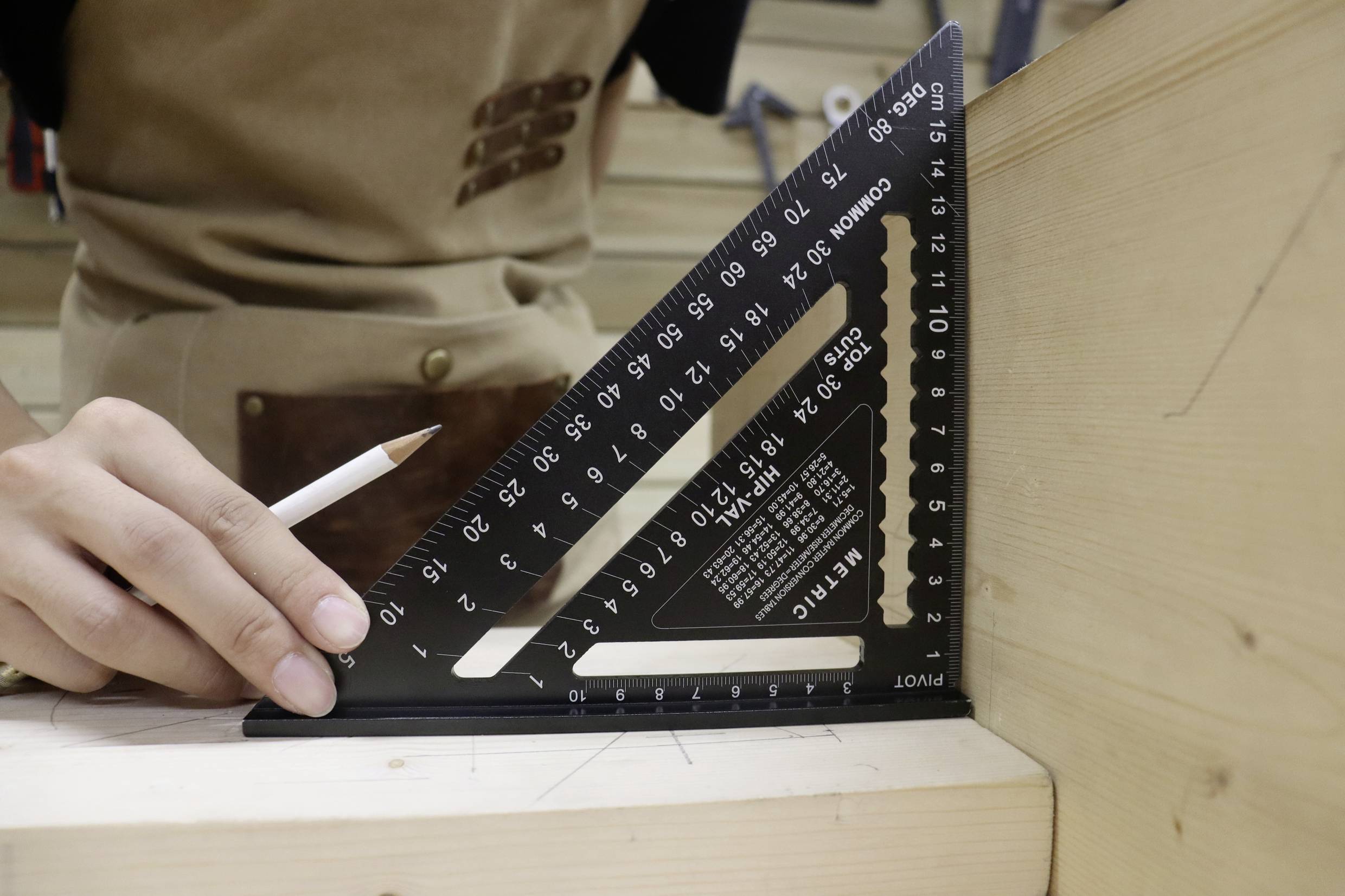 Osoba mierzy czarnym kątomierzem na desce drewnianej, trzymając ołówek w ręku.