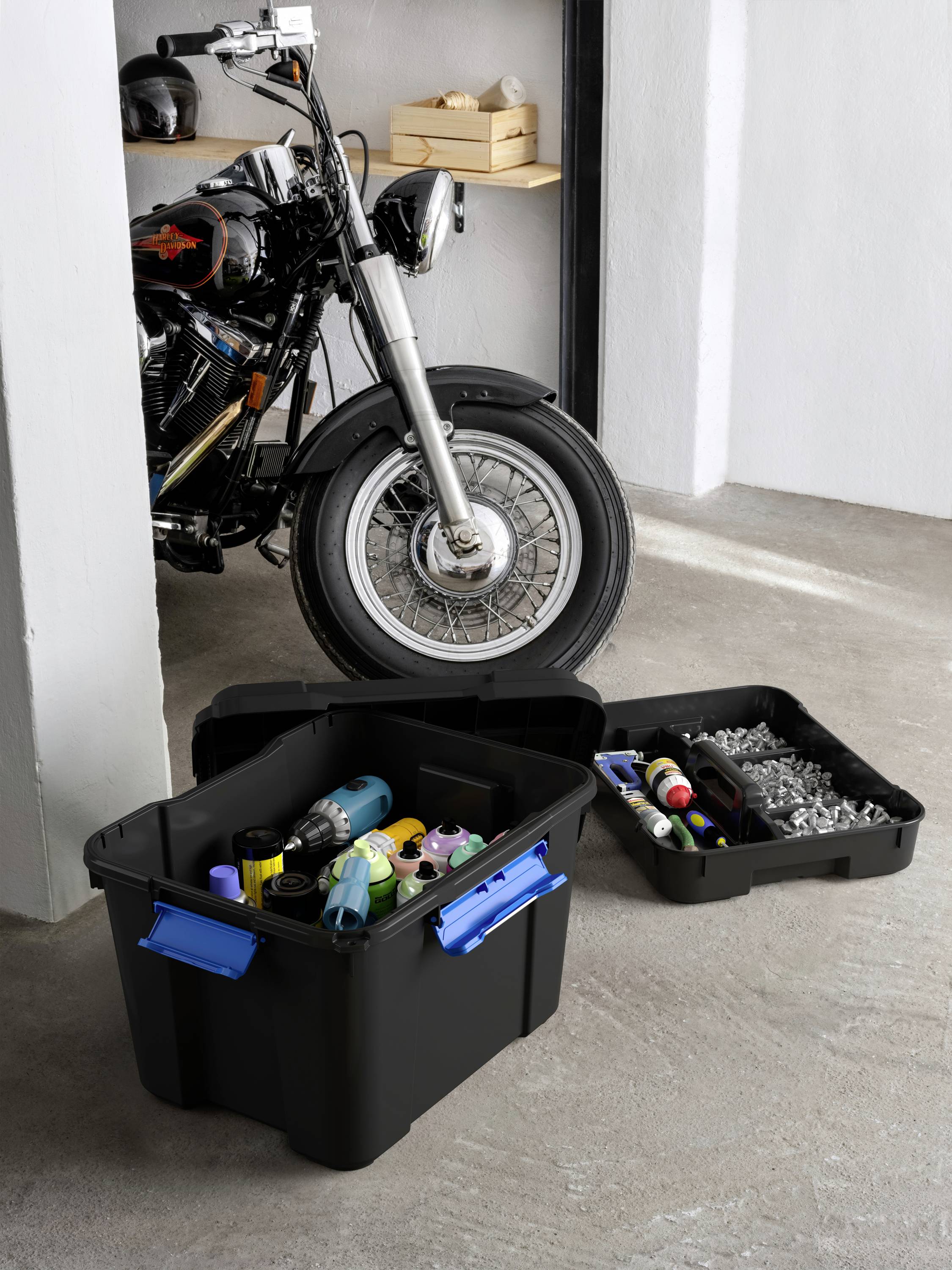 Czarny motocykl stoi w garażu obok dwóch otwartych skrzynek magazynowych. Skrzynki zawierają narzędzia i puszki z farbą w sprayu.