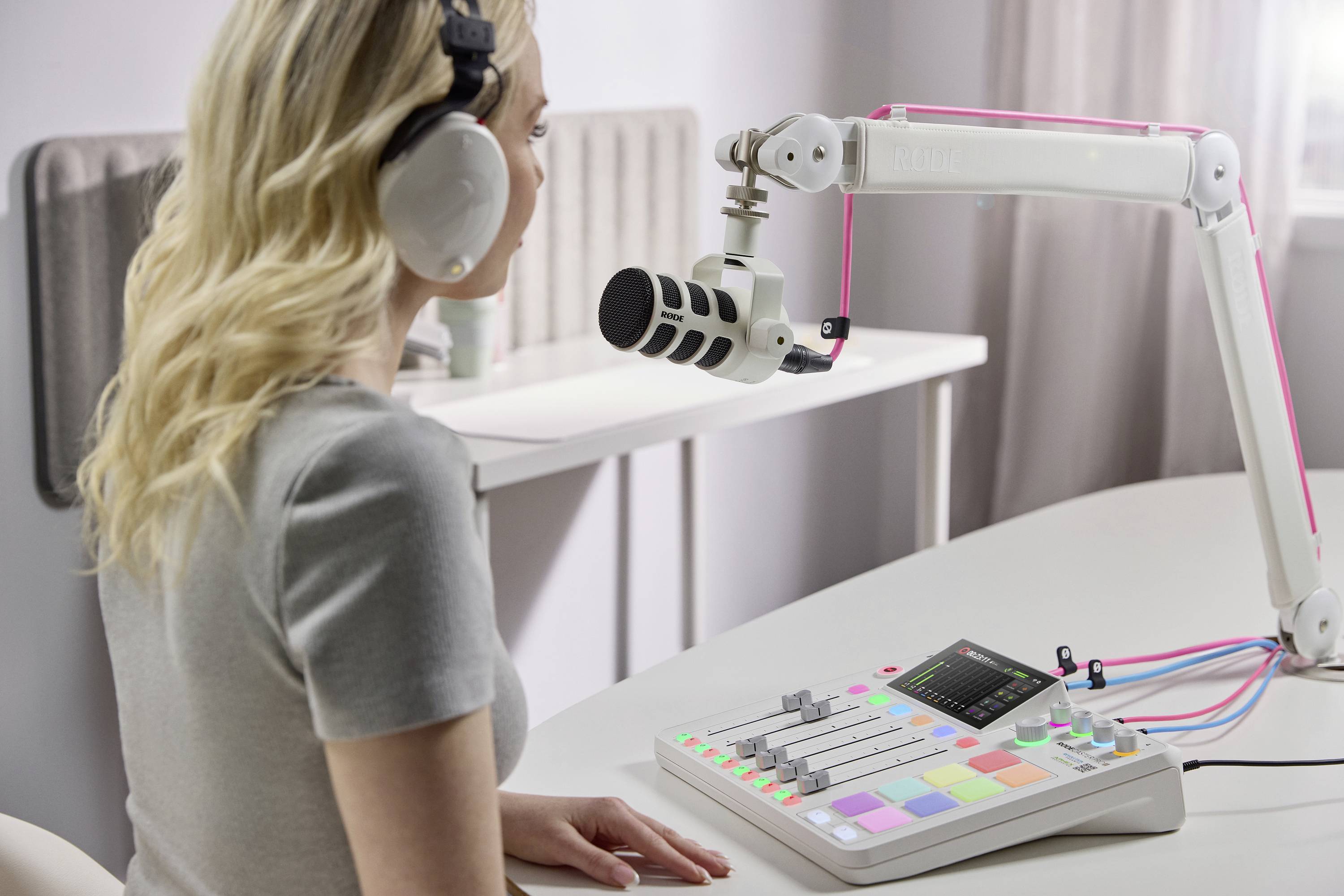 Kobieta w słuchawkach mówi do mikrofonu przed konsolą mikserską. Siedzi w jasnym pomieszczeniu i wydaje się nagrywać.