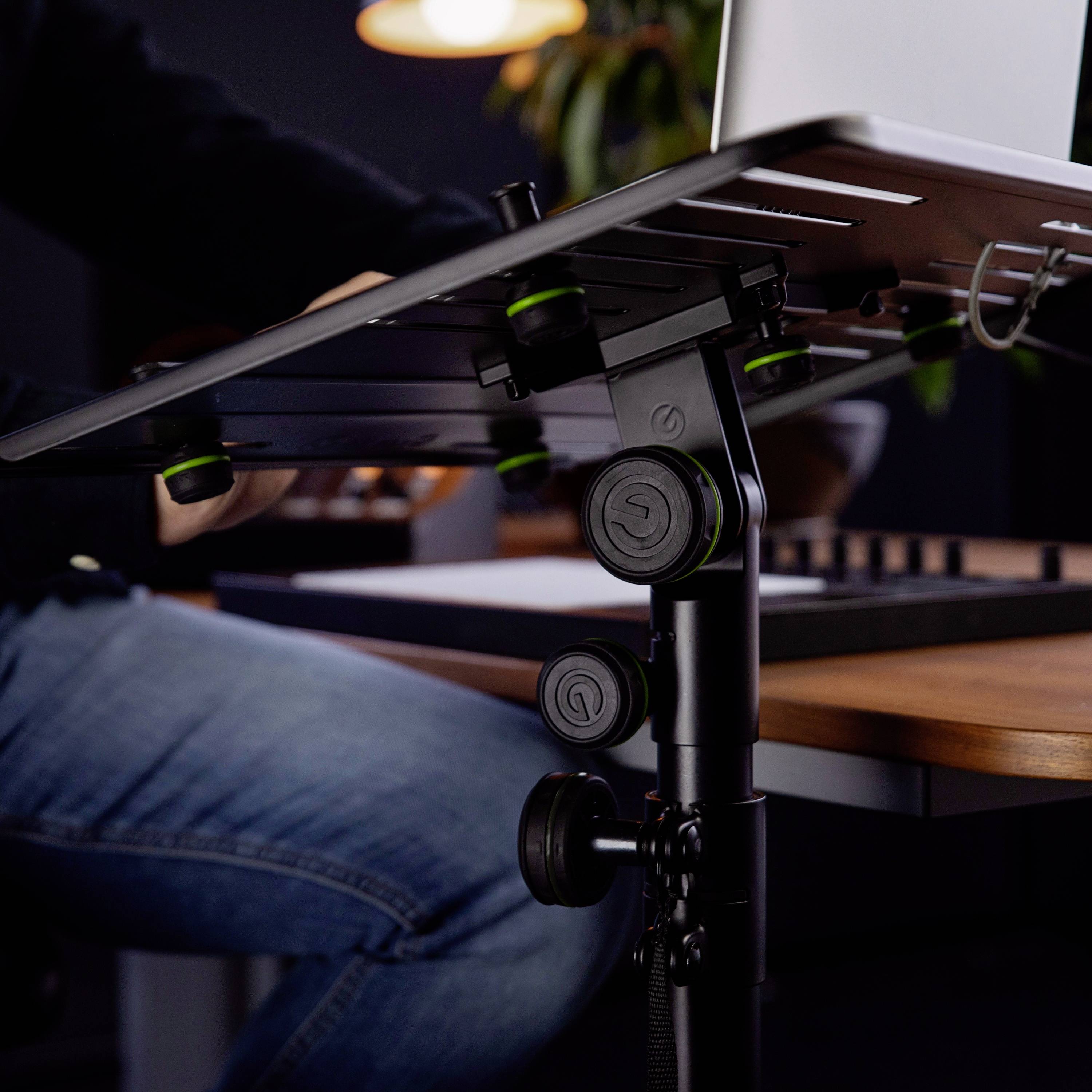 Osoba korzysta z regulowanego na wysokość biurka do pracy na stojąco z laptopem na wierzchu. W tle widać rozmyte wnętrze biura.