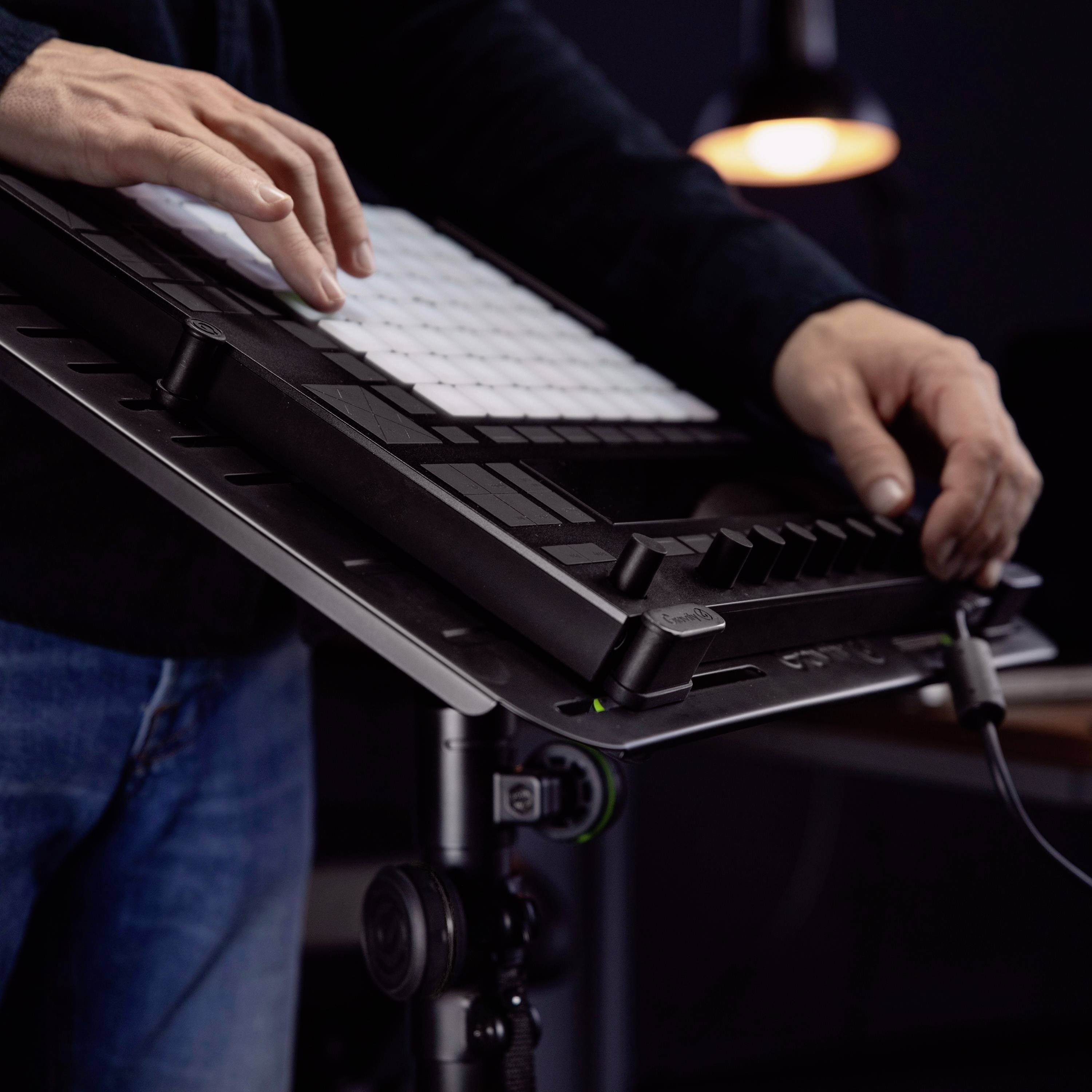 Osoba gra na elektronicznym instrumencie muzycznym z padami w ciemnym pomieszczeniu. W tle włączona jest lampa.