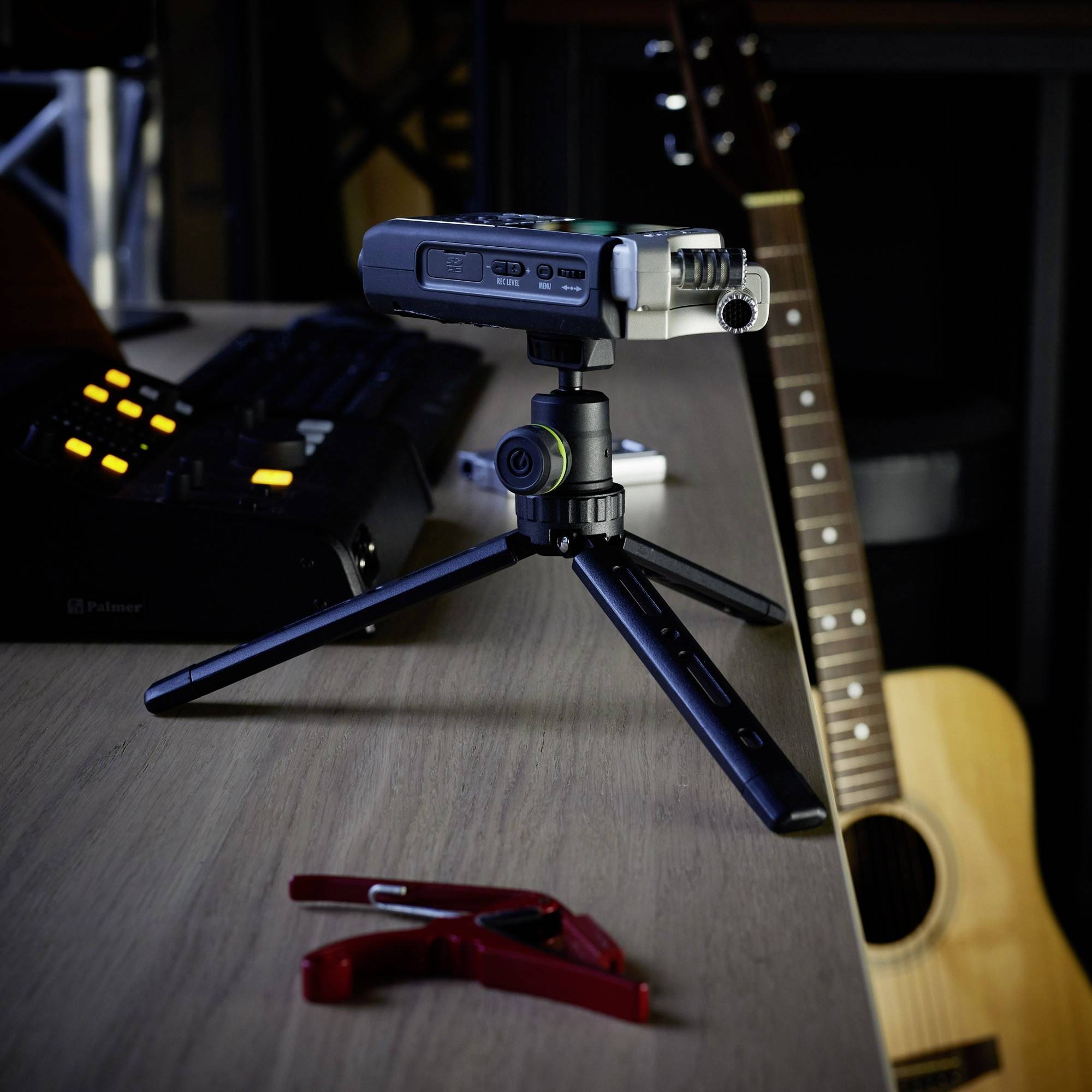 Urządzenie do nagrywania dźwięku na statywie stołowym stoi na biurku. W tle widoczna jest klawiatura i gitara.