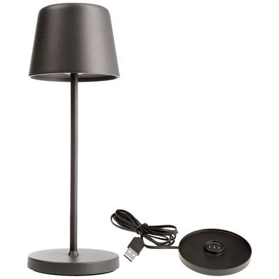 Czarna lampa stołowa o smukłej sylwetce. Obok niej znajduje się podstawa z portem USB do ładowania.