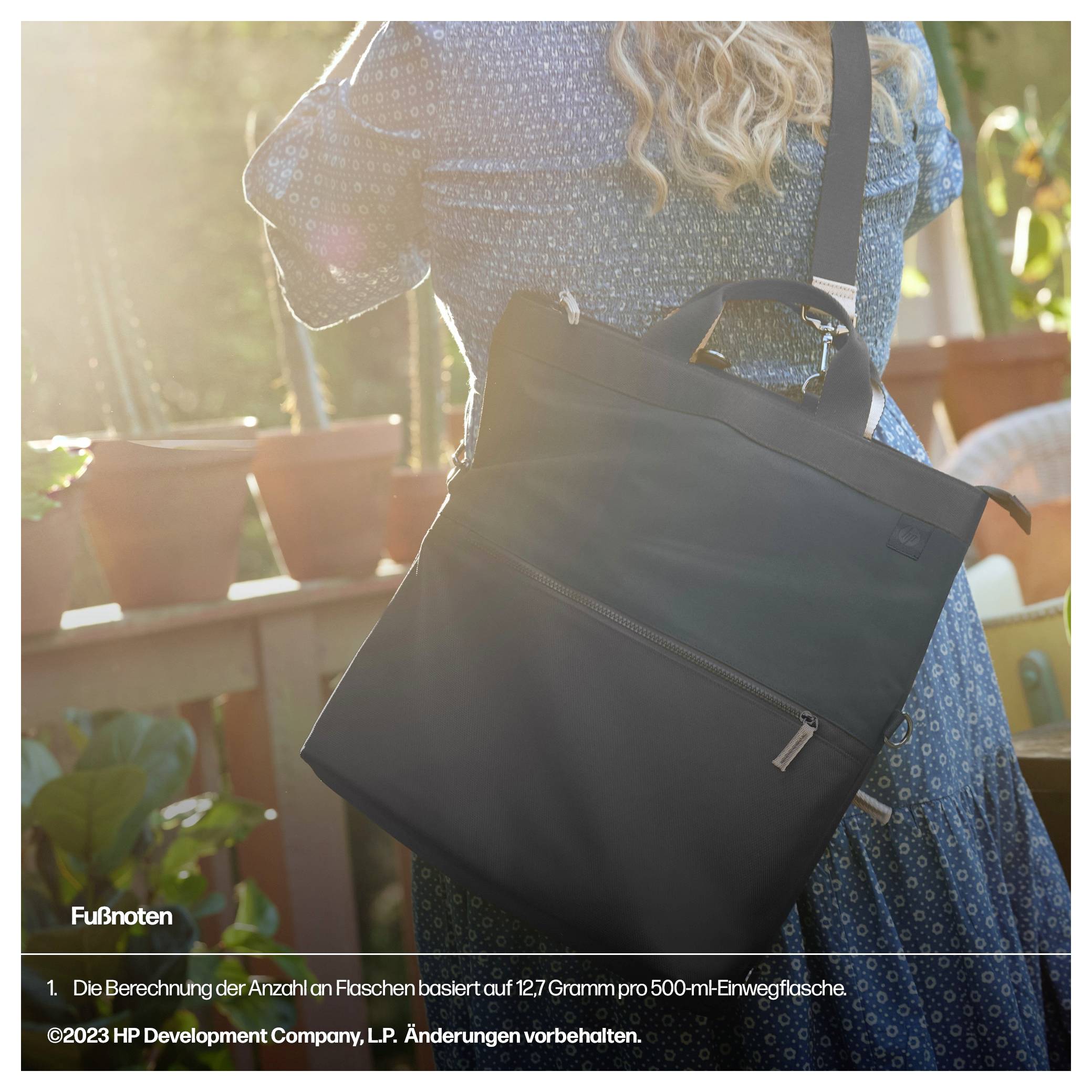 Kobieta nosi czarną torbę przewieszoną przez ramię, stojąc w słonecznym ogrodzie. W tle widoczne są rośliny.