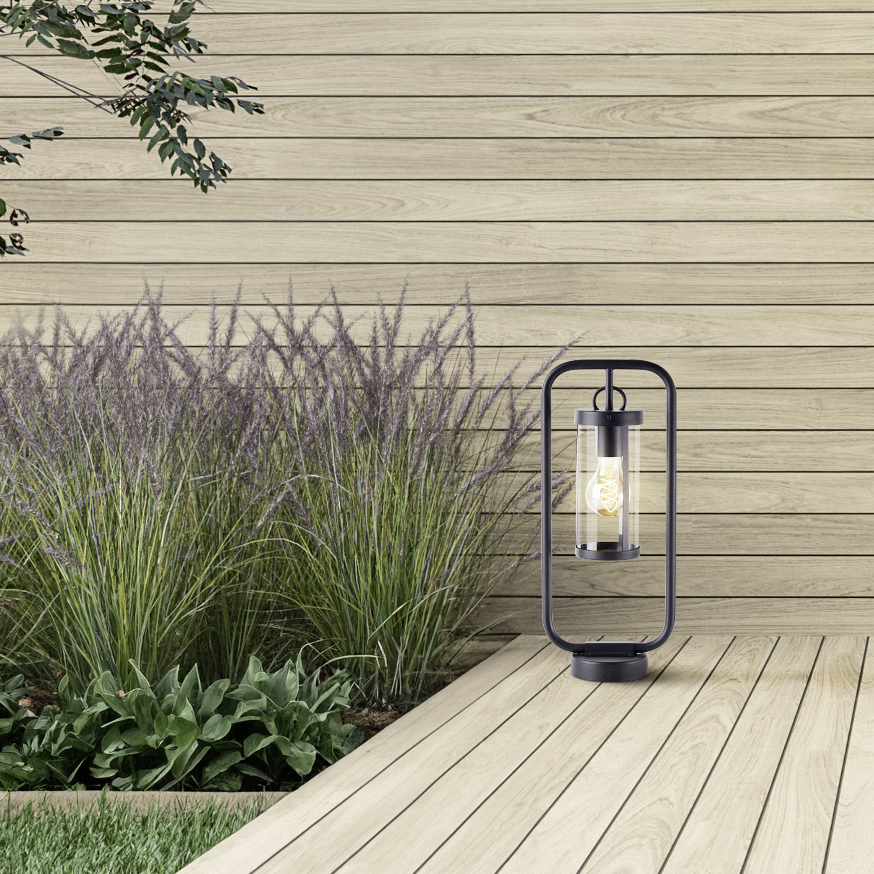 Drewniana terasa z dekoracyjną latarnią obok ozdobnych traw i roślin przed drewnianą ścianą.