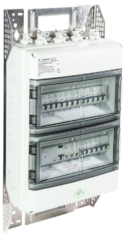 Elektryczna szafa sterownicza z różnymi modułami przełączającymi, oznaczonymi etykietami. Zamontowana na metalowej płycie.