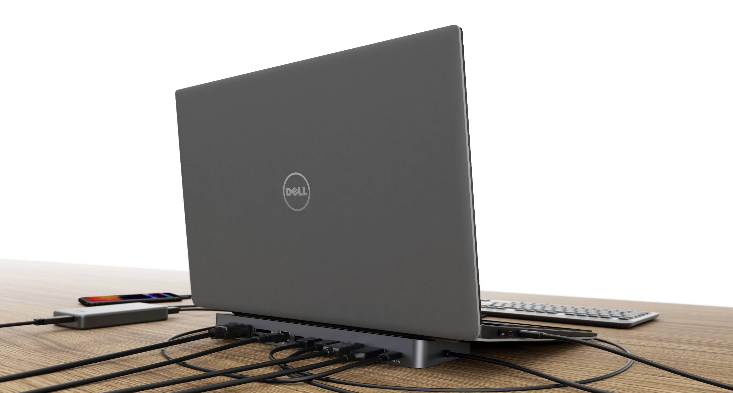 Laptop z podłączonymi wieloma kablami na biurku, obok klawiatura i kabel ładujący.