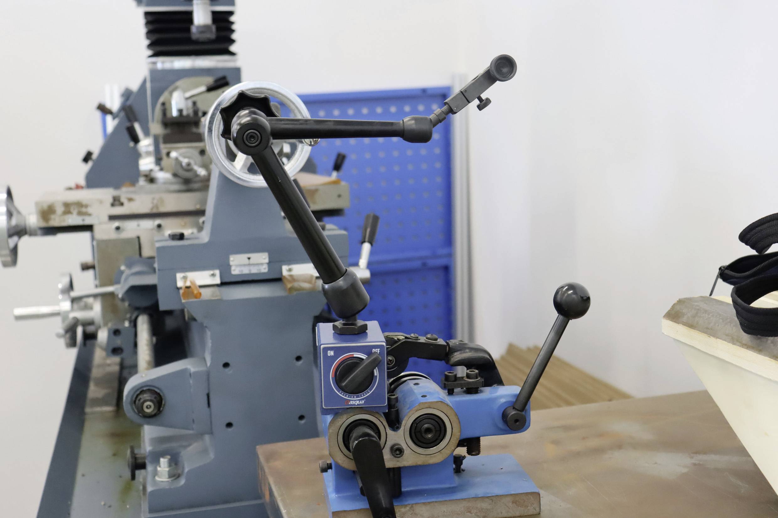Niebieska frezarka z dźwigniami i regulatorami stoi w pomieszczeniu roboczym. W tle widoczne jest kolejne szare urządzenie.