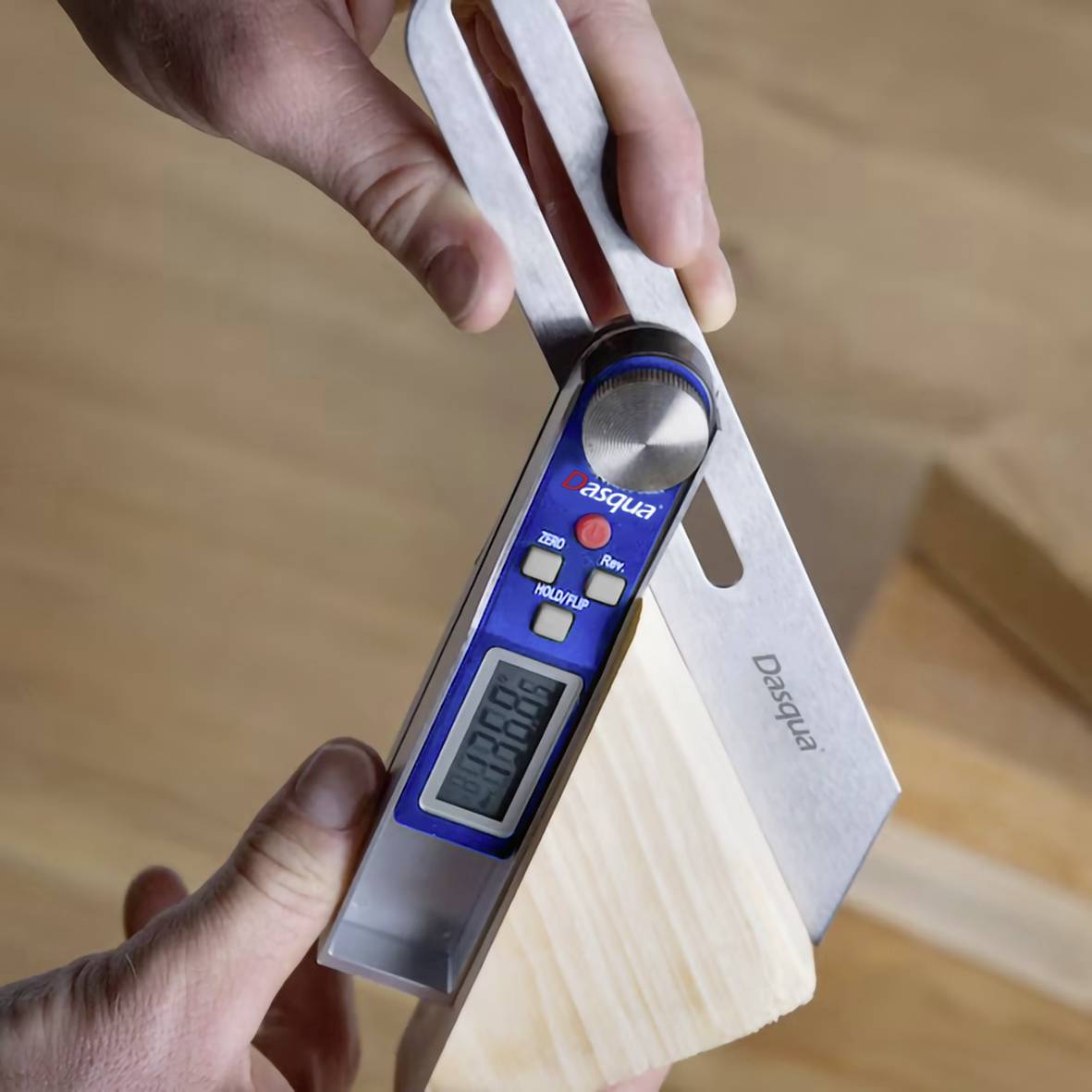 Osoba mierzy kąt kawałka drewna za pomocą cyfrowego kątomierza. Wyświetlacz pokazuje aktualną wartość kąta.