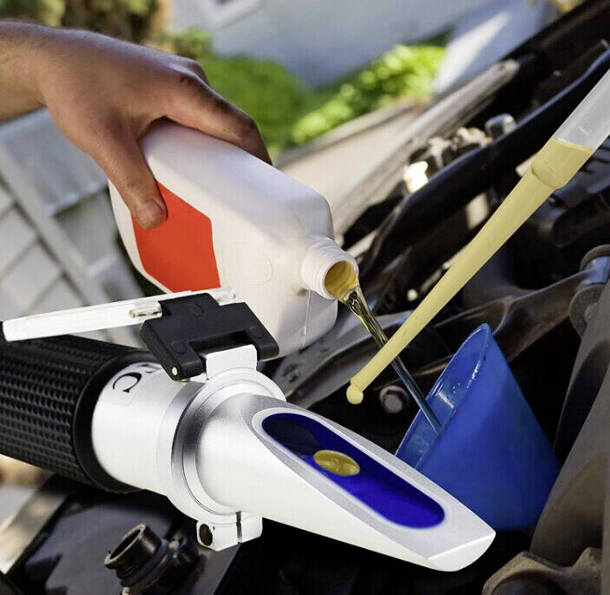 Osoba wlewa olej silnikowy do samochodu, podczas gdy obok używany jest refraktometr do sprawdzenia jakości oleju.