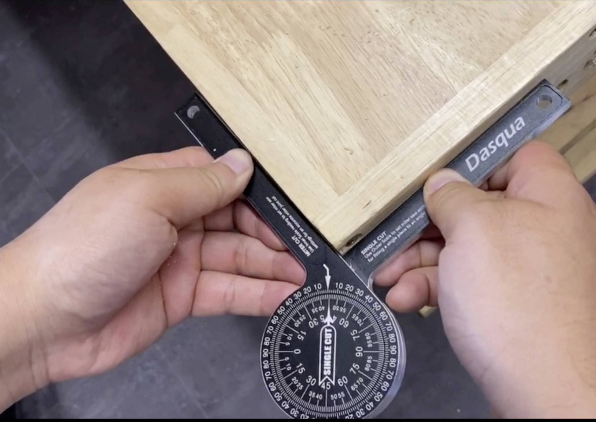 Osoba mierzy kąt drewnianego stołu kątomierzem. Wyświetlacz pokazuje niemal 90 stopni, co wskazuje na kąt prosty.