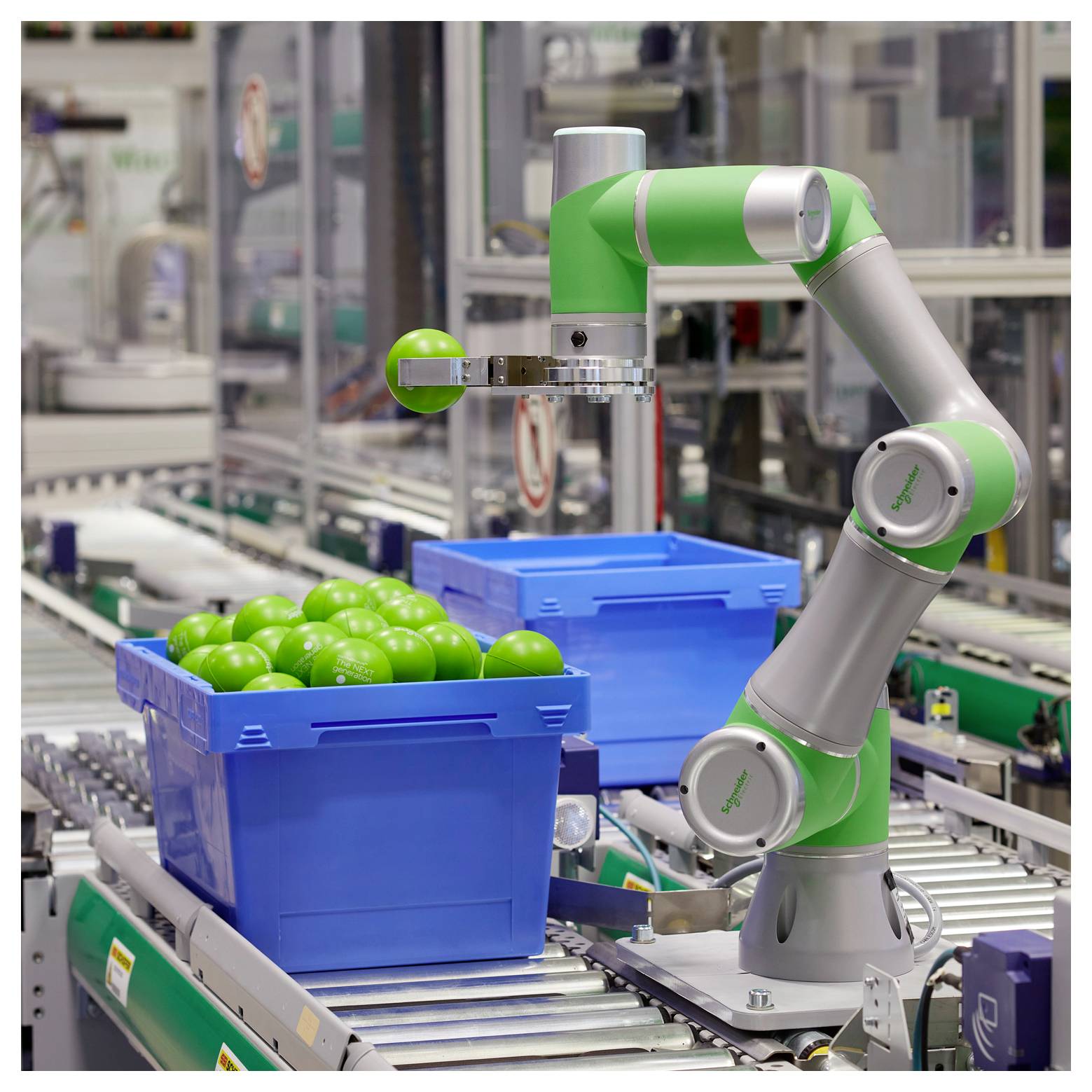 Zielono-srebrne roboty czę ść ramienia zbiera zielone jabłko z niebieskiego pojemnika na taśmie przenośnika w automatycznej linii produkcyjnej fabryki.