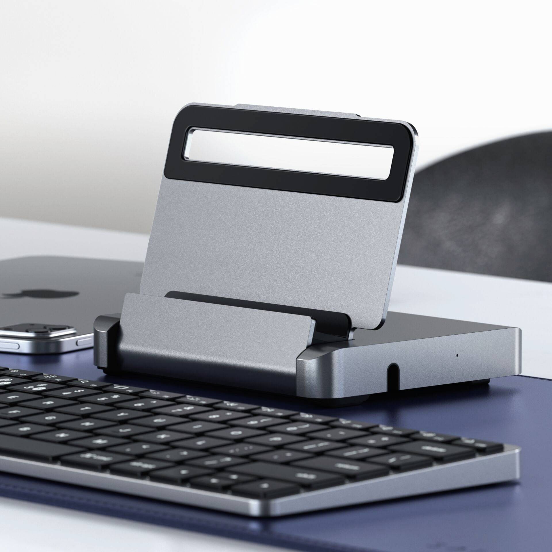 Tablet stoi na podstawce za klawiaturą, obok smartfona na biurku.