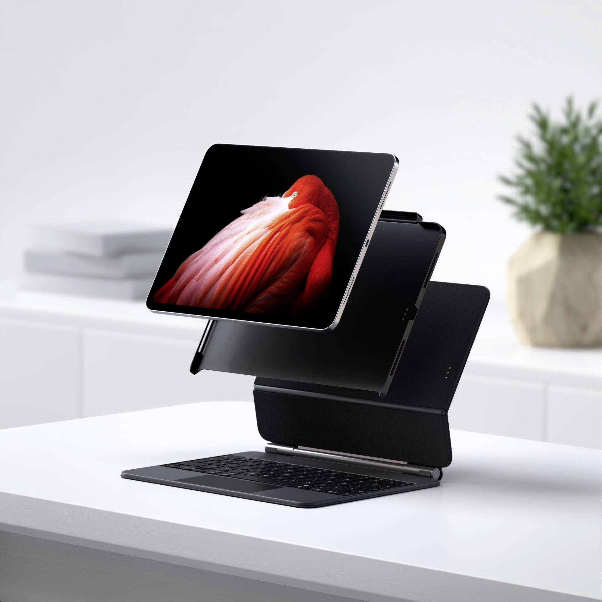 Tablet unosi się nad klawiaturą na biurku. W tle stoi zamknięty laptop i roślina.