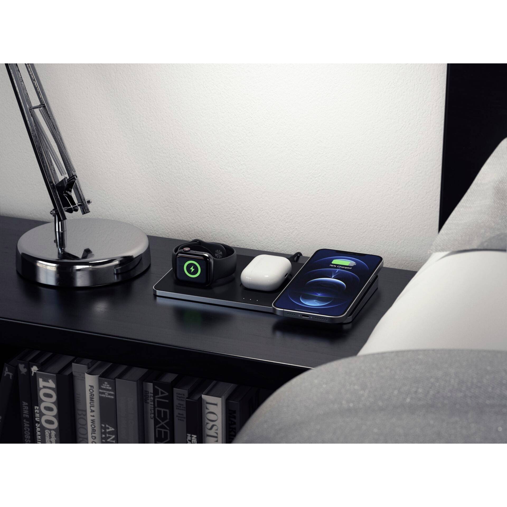 Stolik nocny z lampką, smartwatchem, bezprzewodowymi słuchawkami dousznym i smartfonem leżącym na stacji ładującej.