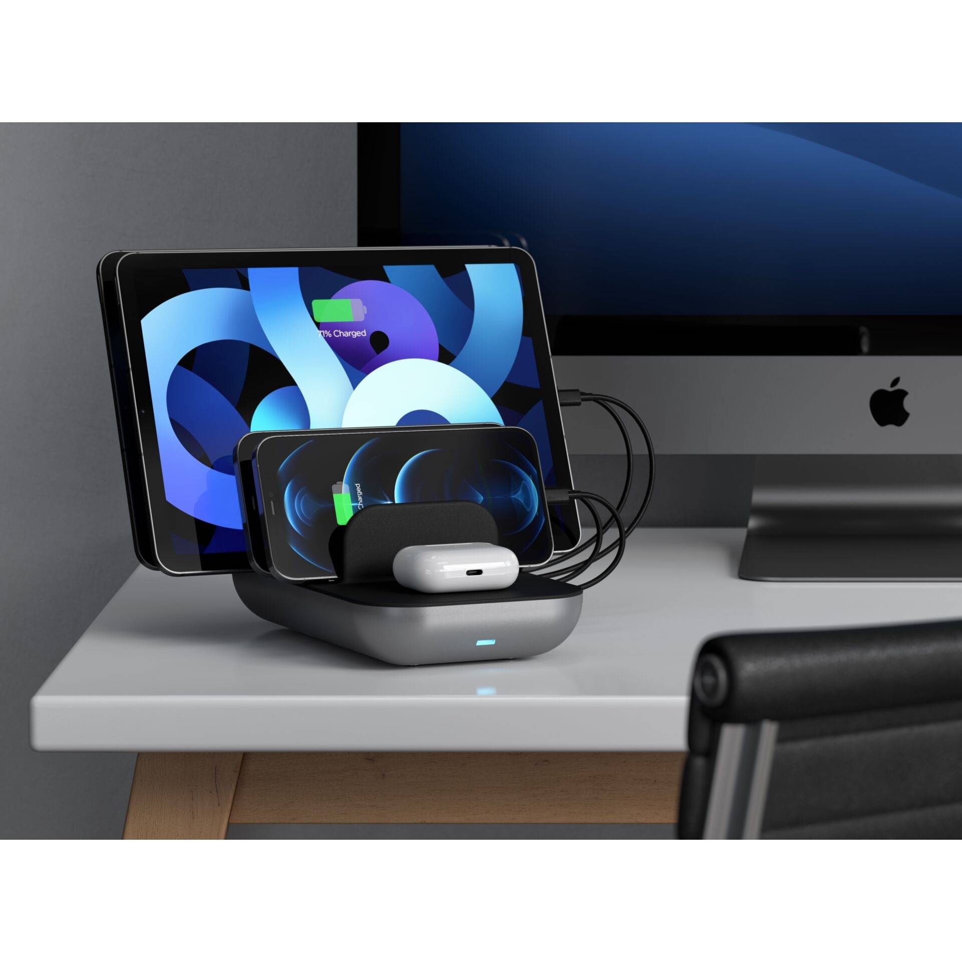 Smartfon, smartwatch i AirPodsy ładują się bezprzewodowo na stacji ładującej obok ekranu tabletu i komputera.