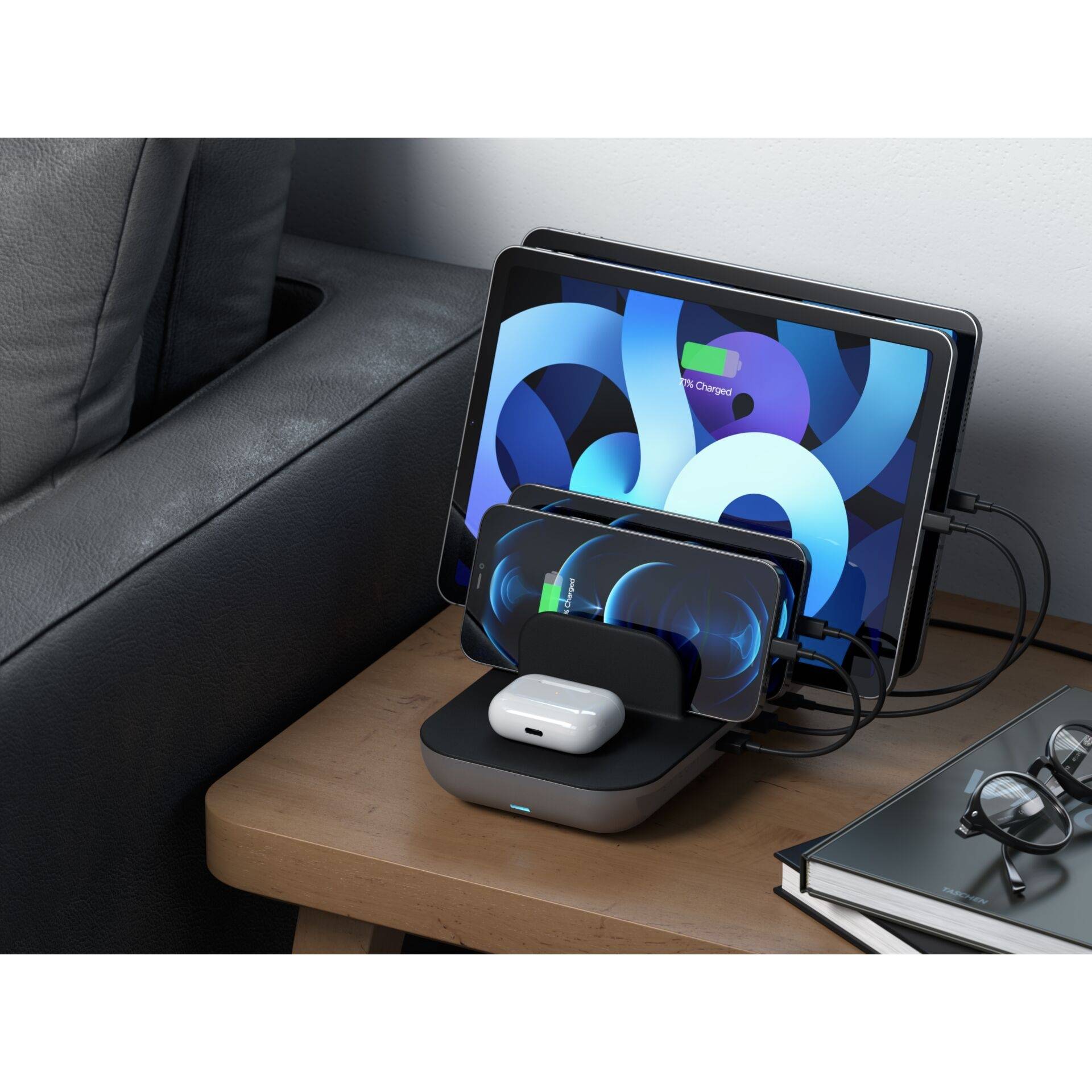 Tablet, smartfon i słuchawki są bezprzewodowo ładowane na drewnianym stole. Obok leżą okulary i książka.