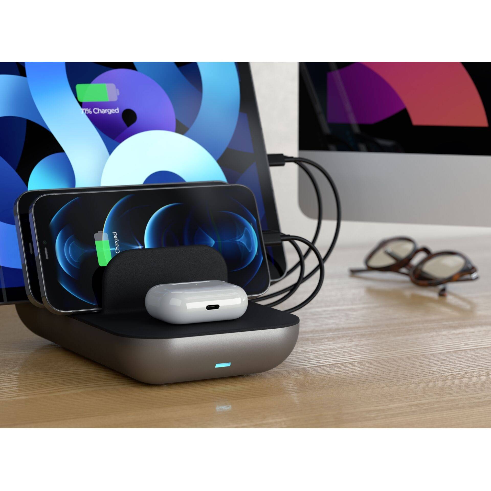 Bezprzewodowa ładowarka ładuje smartfon i bezprzewodowe słuchawki. W tle widoczny jest monitor i okulary.