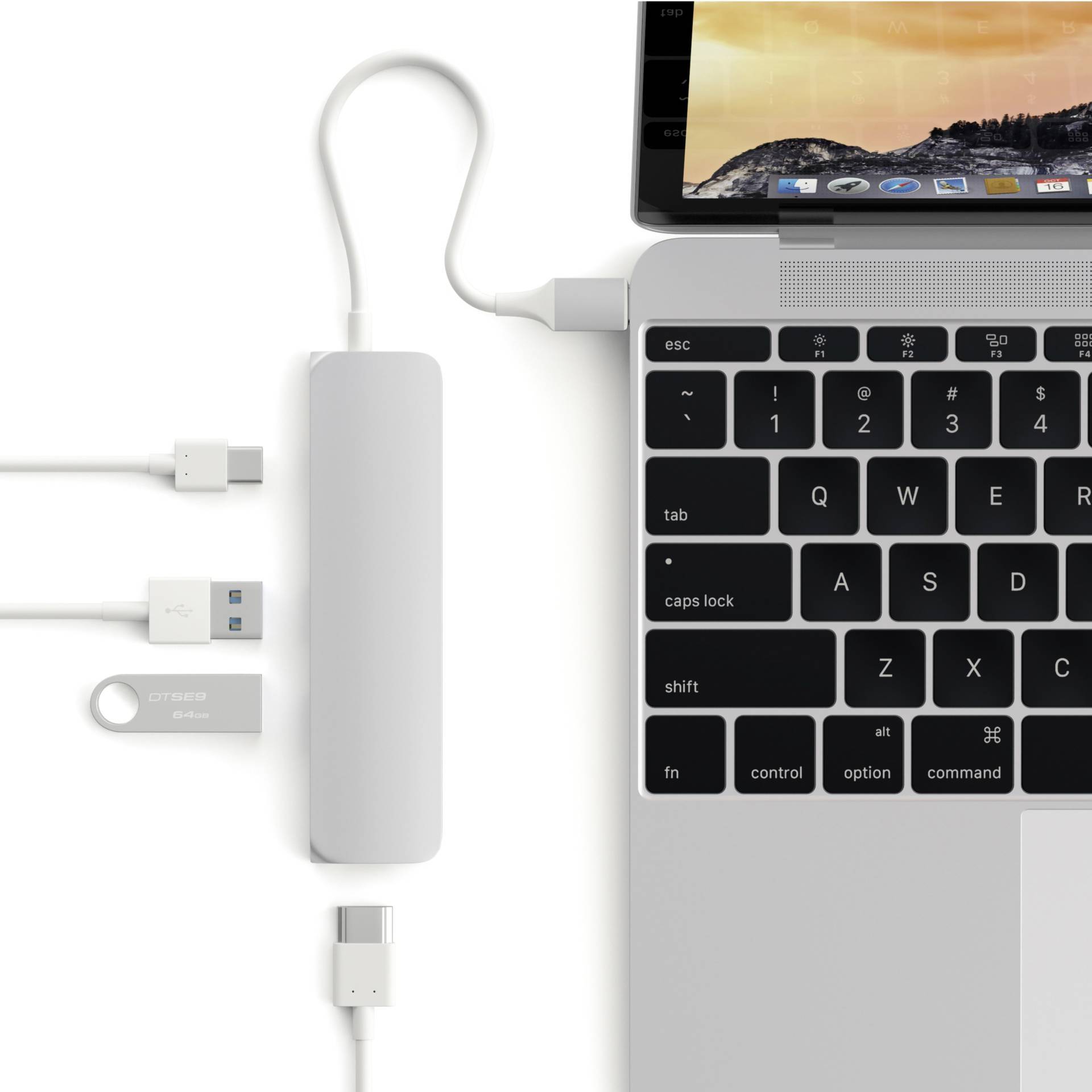 Laptop jest podłączony do koncentratora USB-C, do którego podłączonych jest kilka urządzeń USB. Na ekranie laptopa widoczne jest tło przedstawiające zachód słońca.