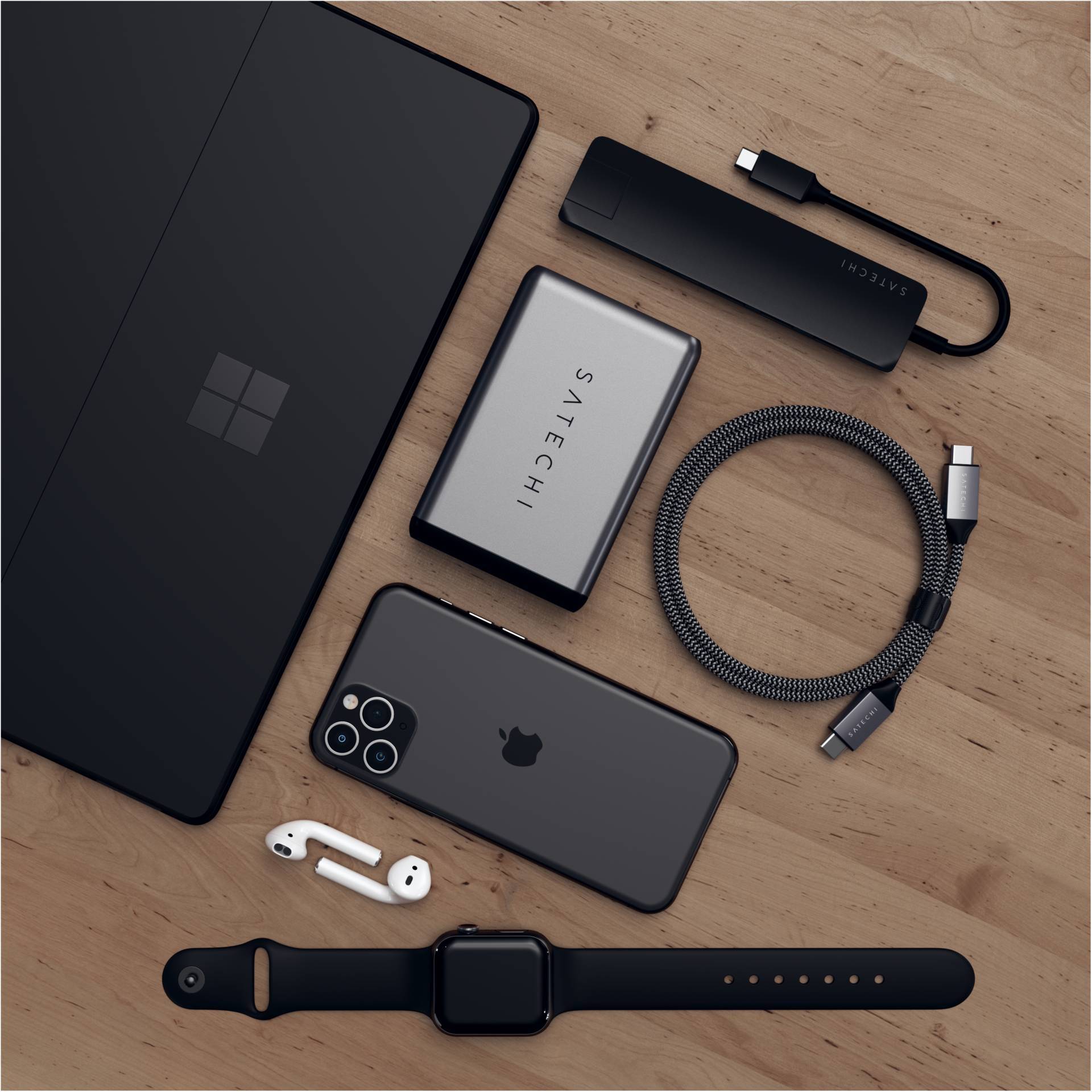 Laptop, smartfon, przenośny dysk twardy, hub USB, kabel pleciony, bezprzewodowe słuchawki douszne i smartwatch na drewnianym stole.