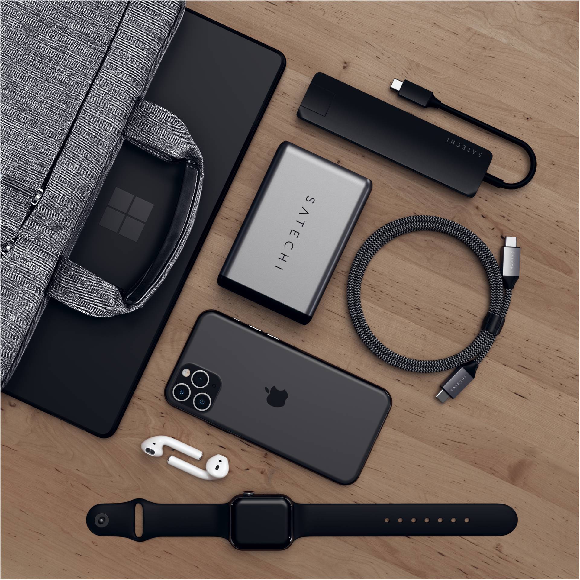 Elektroniczne urządzenia na drewnianym stole: laptop, smartfon, ładowarki, kable, słuchawki, smartwatch. Układ do podróży lub pracy.