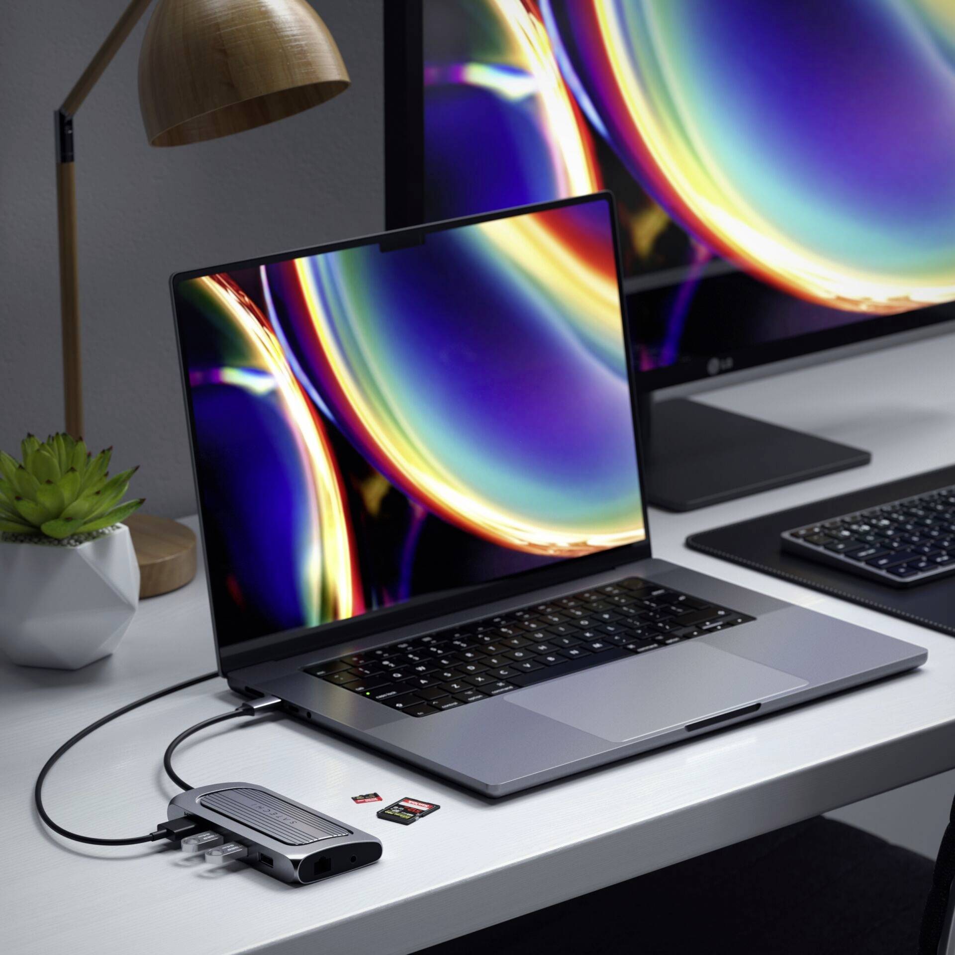 Laptop stoi na biurku. Do laptopa podłączona jest stacja dokująca z kablami i kartami pamięci.