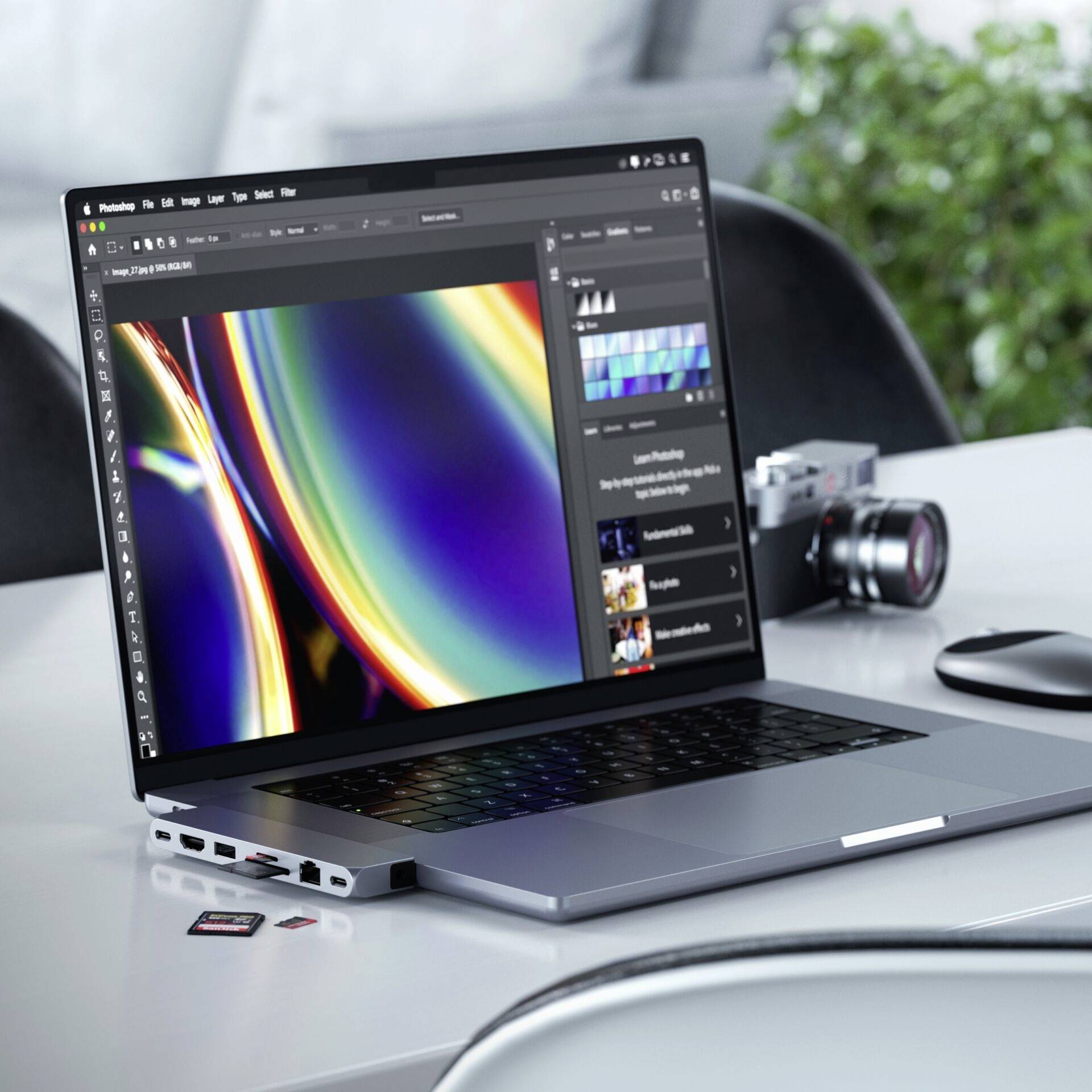 Laptop na biurku z programem do edycji grafiki wyświetlanym na ekranie. Obok leży aparat fotograficzny i karty SD.