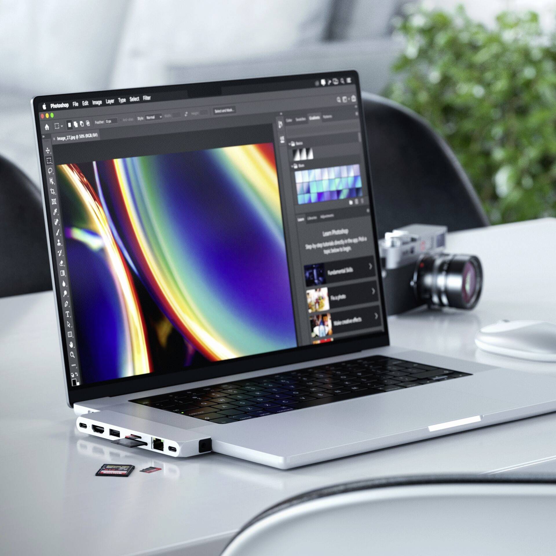Laptop z otwartym programem do edycji zdjęć wyświetla abstrakcyjny, tęczowy design. Obok niego aparat fotograficzny i karty pamięci.