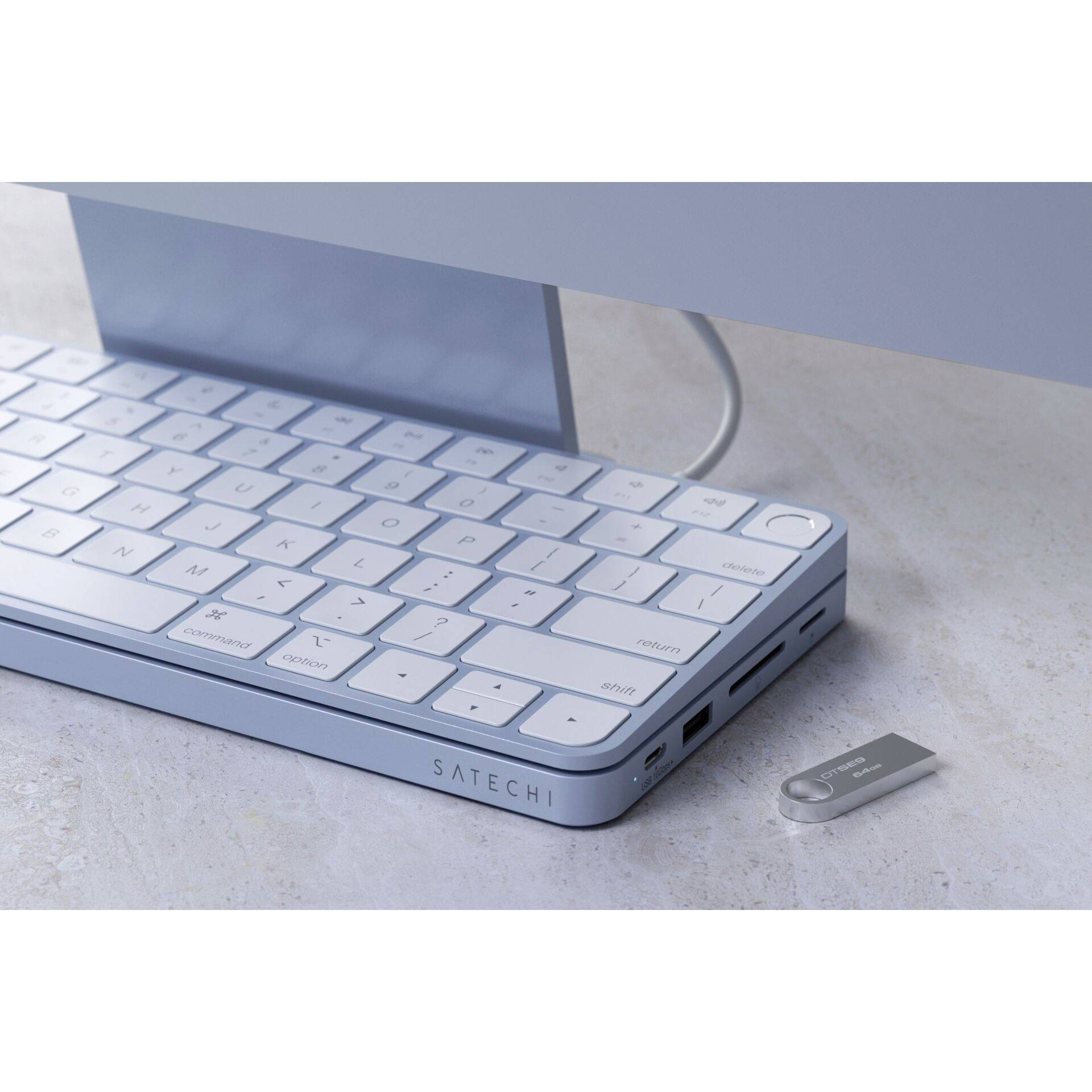 Niebieska klawiatura z podłączeniem USB na biurku, obok pendrive. Widoczny napis 'SATECHI'. Na dole obrazka przewód komputerowy.