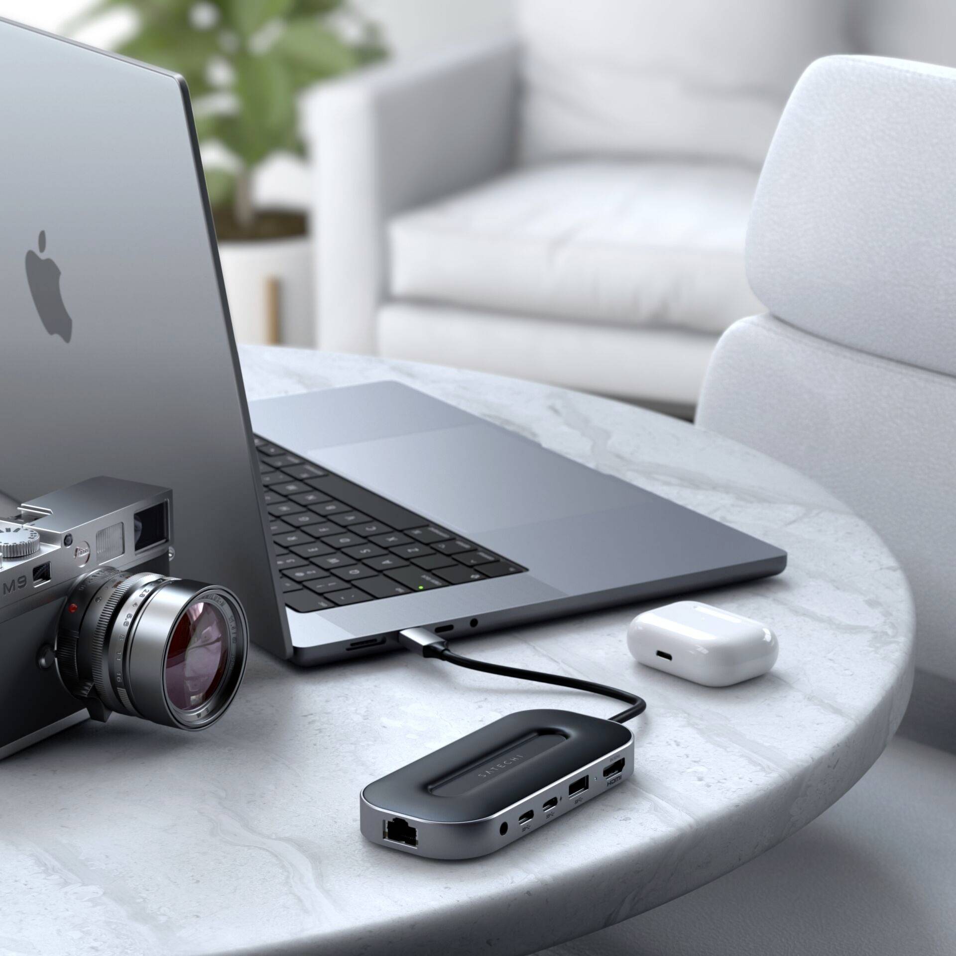 Laptop, aparat fotograficzny i bezprzewodowe słuchawki douszne na okrągłym stole w salonie. W tle rozmyty fotel.