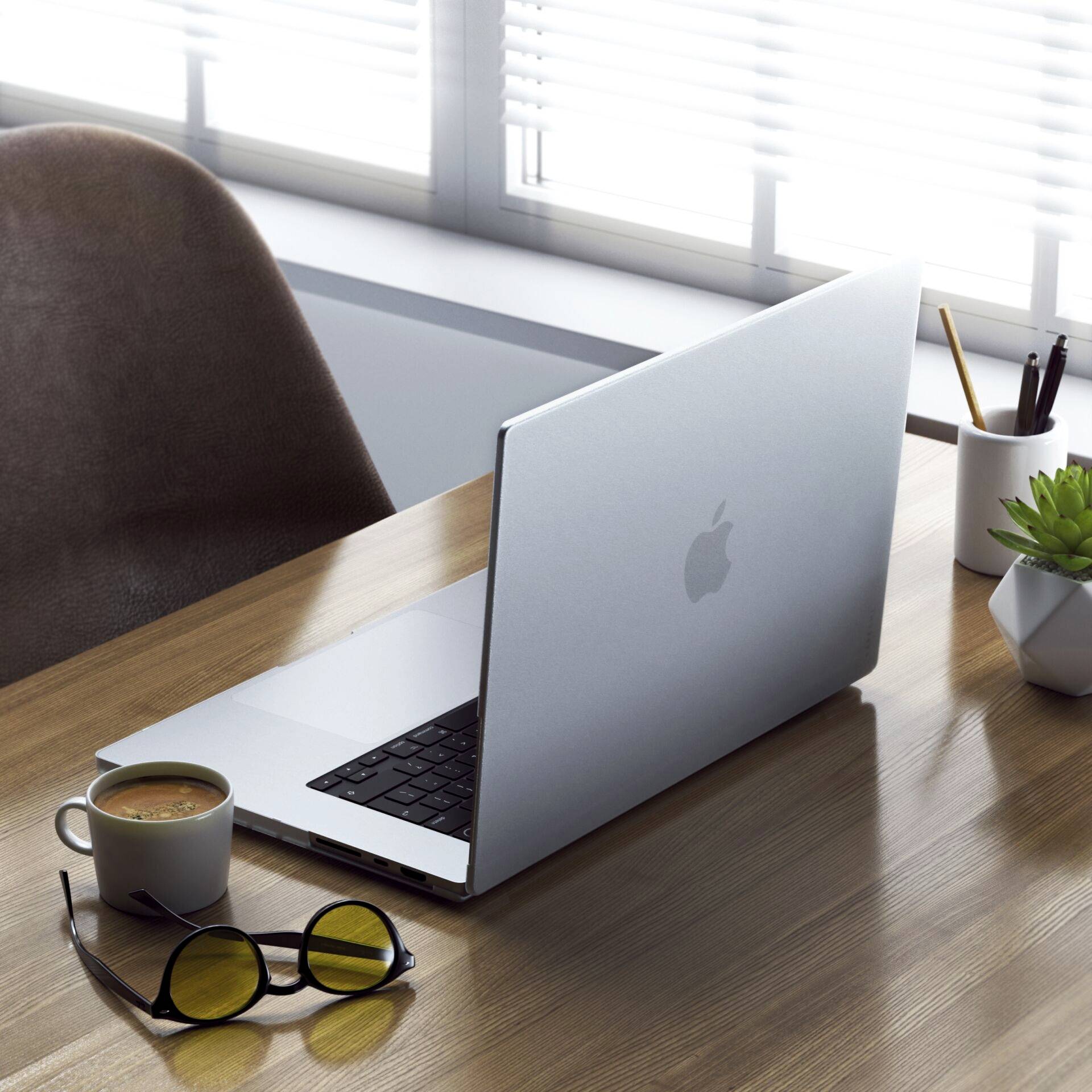 Laptop stoi na biurku obok okularów i doniczki z rośliną. W tle widać okno z zasłoniętymi żaluzjami.