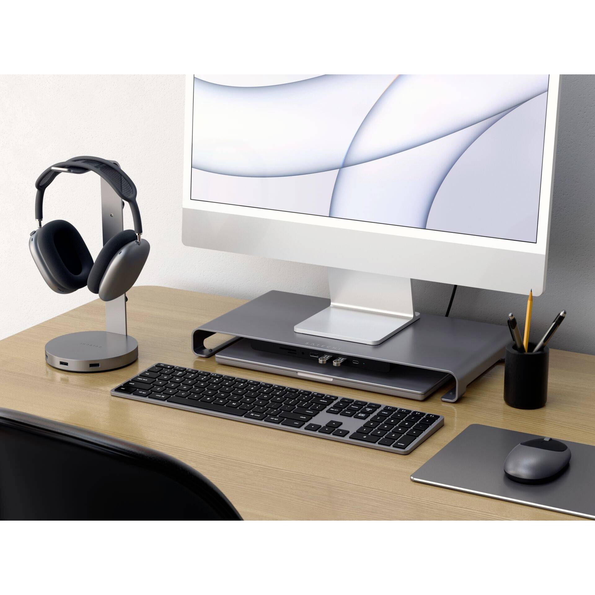 Stanowisko pracy z komputerem, stojakiem na słuchawki, klawiaturą i myszą na drewnianym stole.