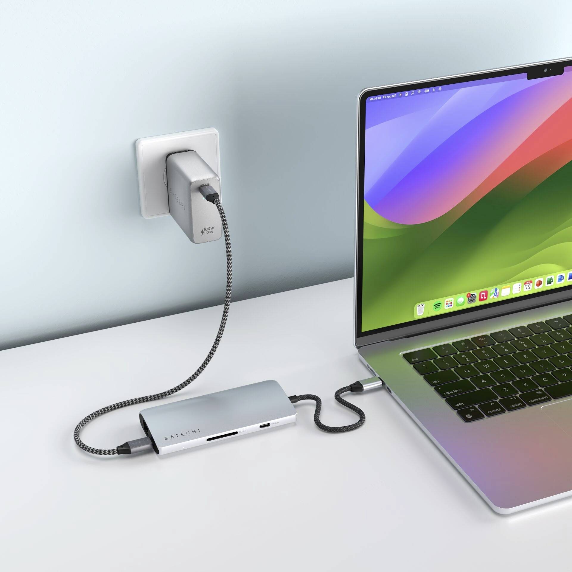 Laptop jest podłączony do zasilacza za pomocą koncentratora USB-C, który jest wpięty w gniazdko elektryczne. Na ekranie wyświetlają się kolorowe fale.