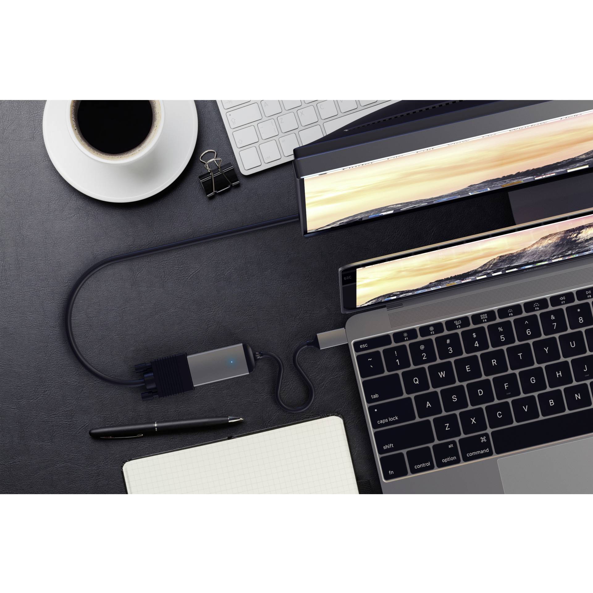 Stanowisko pracy z laptopem, dwoma monitorami, kubkiem kawy, notatnikiem i długopisem. Monitory wyświetlają krajobraz i są ze sobą połączone.