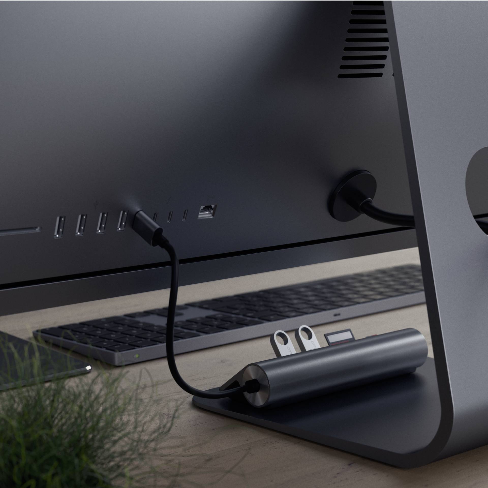 Komputer o smukłej sylwetce stoi na biurku, tyłem do widza, z podłączonymi kablami i klawiaturą w tle.