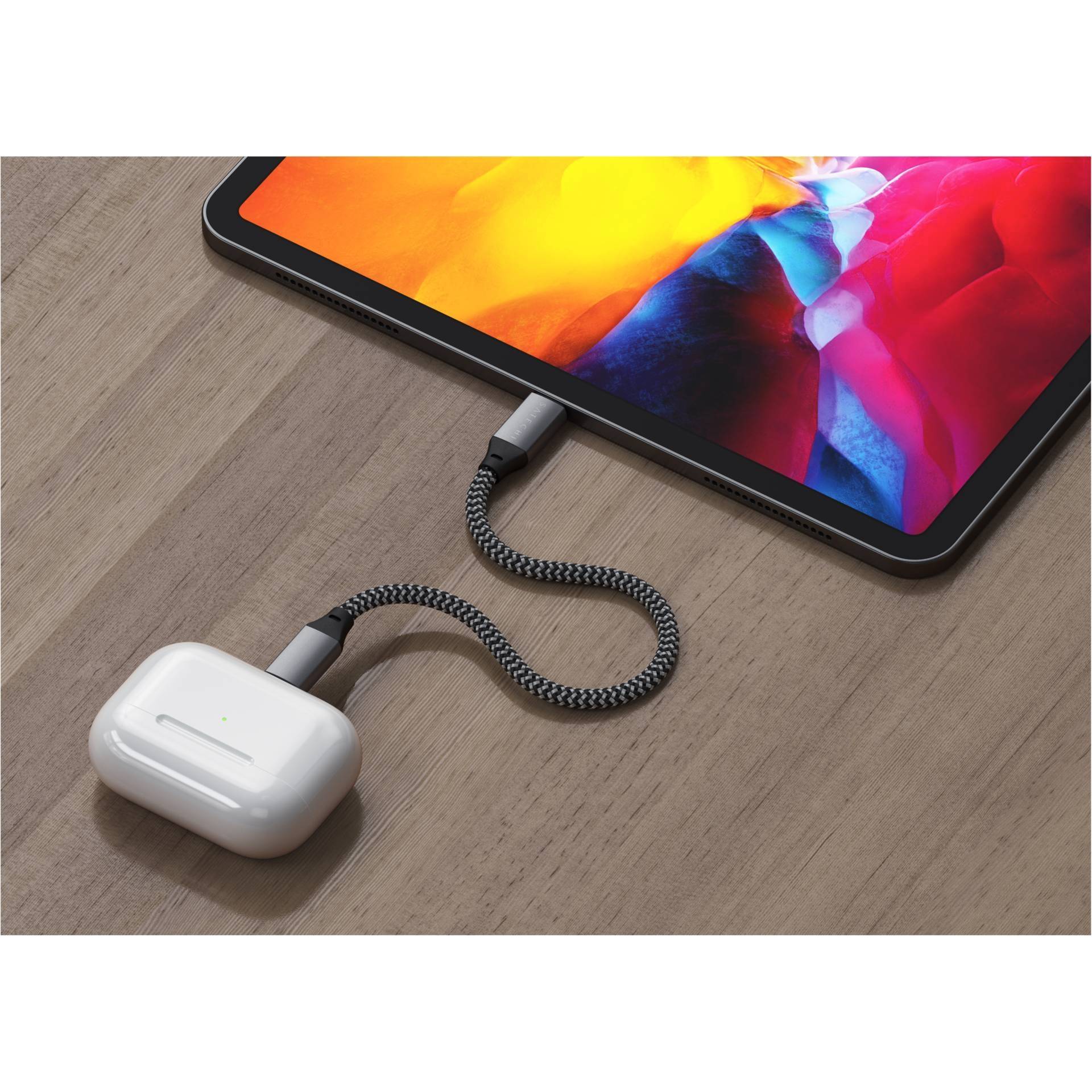 Tablet z podświetlonym ekranem jest podłączony plecionym przewodem do bezprzewodowych słuchawek dousznych, leżący na drewnianym stole.