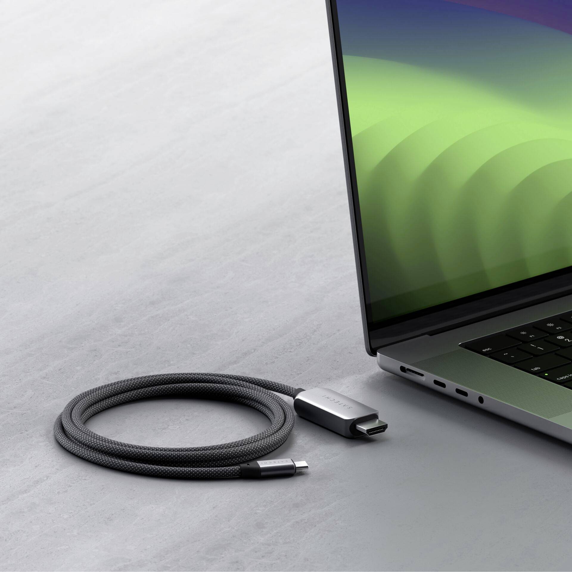 Laptop z zielonym ekranem stoi na stole. Obok niego leży czarny kabel ładujący z wtyczką USB-C.