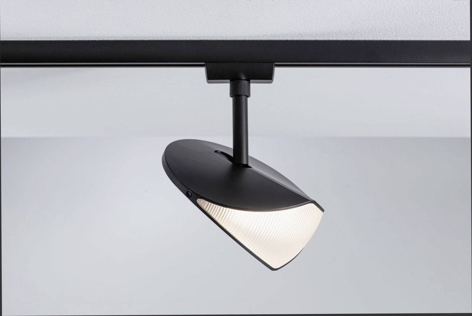 Czarny spot sufitowy z stożkowatym kloszem emituje jasne światło i jest zamontowany na białym suficie.