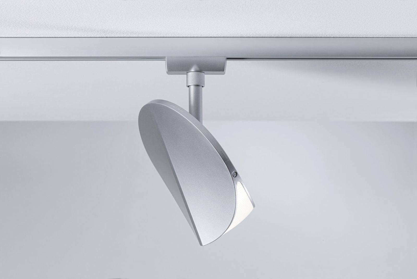 Nowoczesna, srebrna lampa sufitowa o zaokrąglonym kształcie, zamontowana na szynie przy suficie.