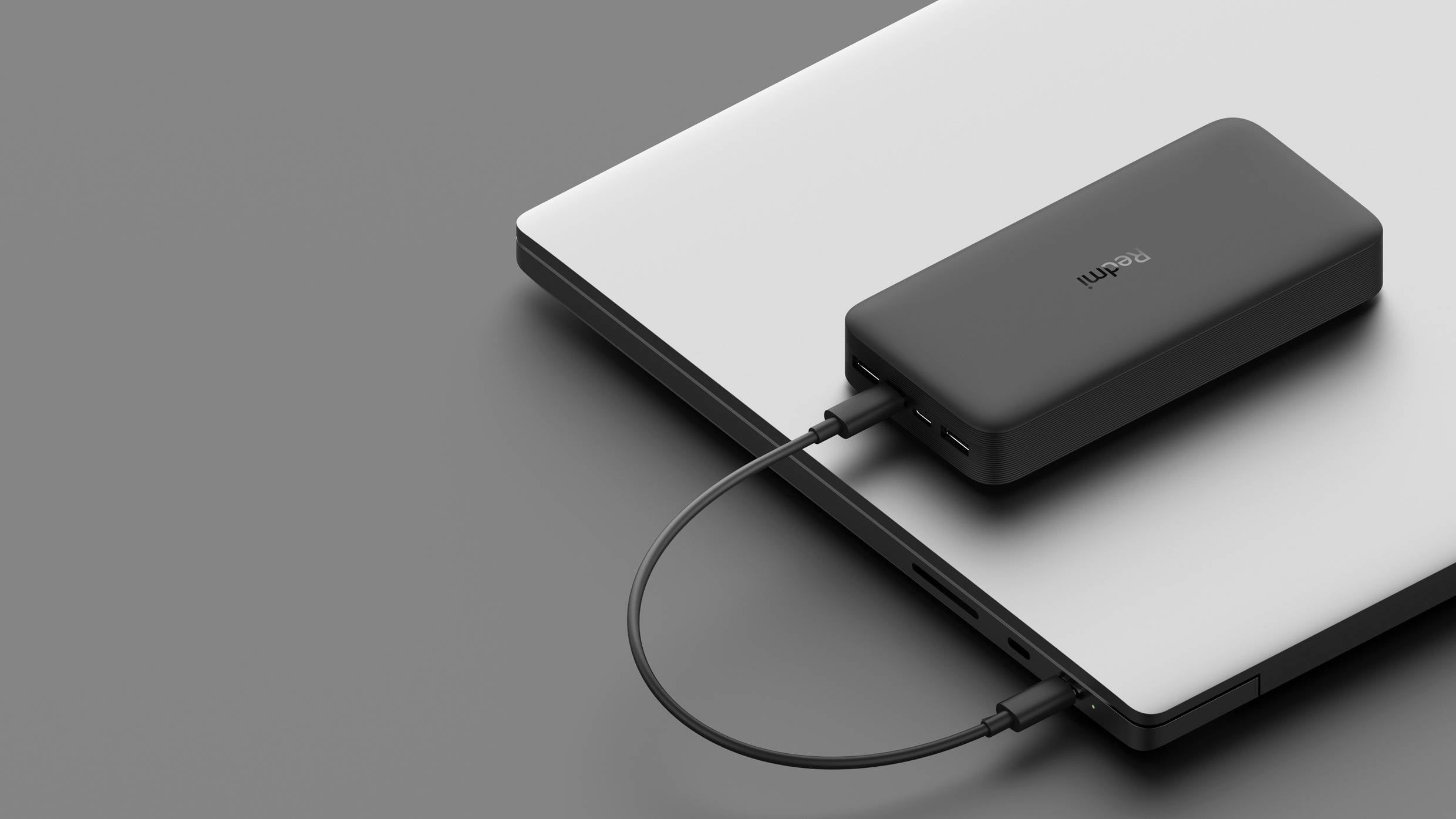 Czarny power bank leży na laptopie i jest podłączony przewodem, co ilustruje mobilność i wsparcie technologiczne.