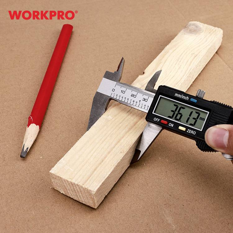 Cyfrowy suwmiarz mierzy kawałek drewna. Wartość na wyświetlaczu wynosi 36,13 mm. Obok leży czerwony ołówek.