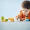 Małe dziecko siedzi na podłodze i bawi się kolorowymi klockami oraz figurkami zwierząt. Tło jest jasnoniebieskie.