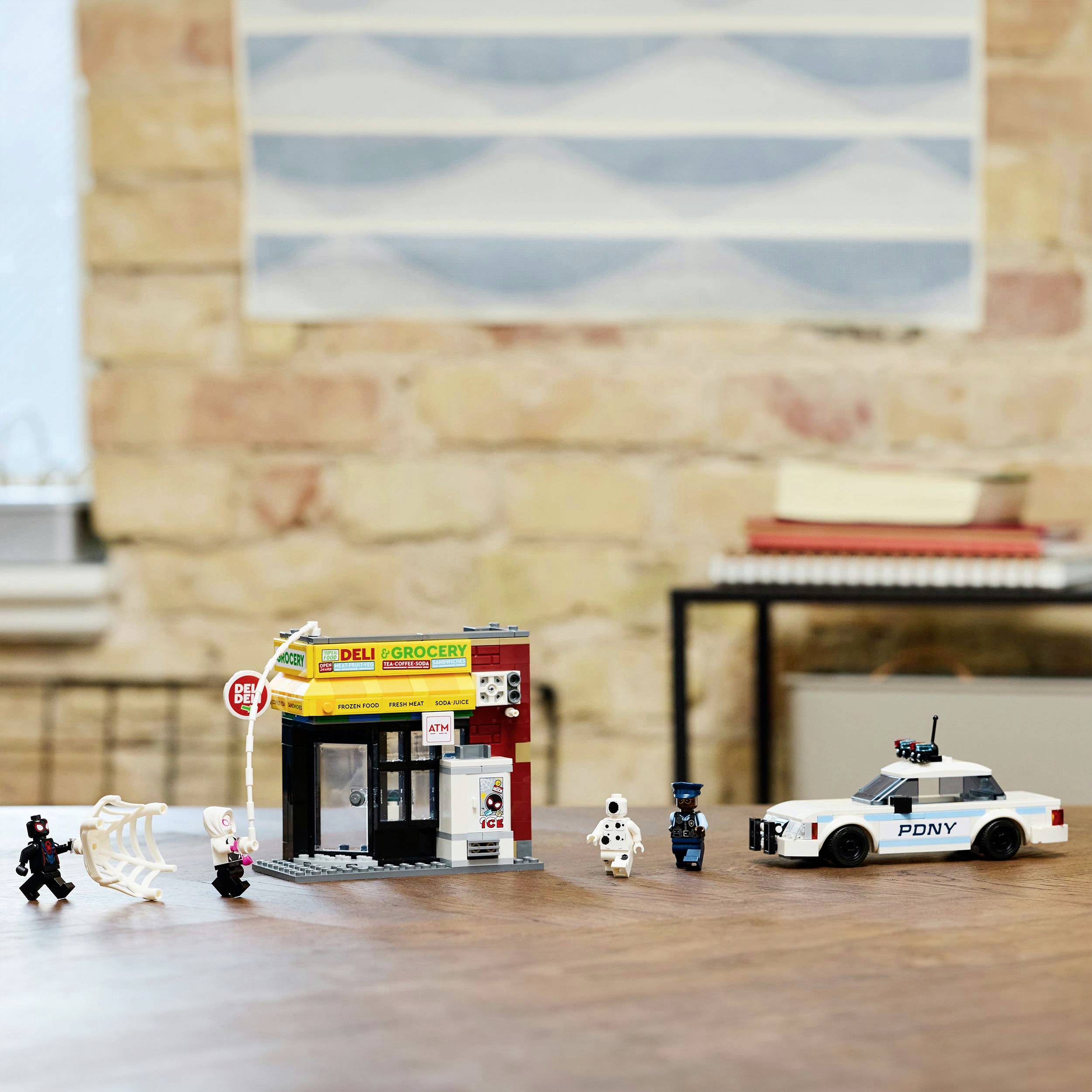 Scena z klocków Lego przedstawia małą sklepik spożywczy oraz białe zabawkowe auto policyjne obok miniaturowych figurek w jednym pomieszczeniu.