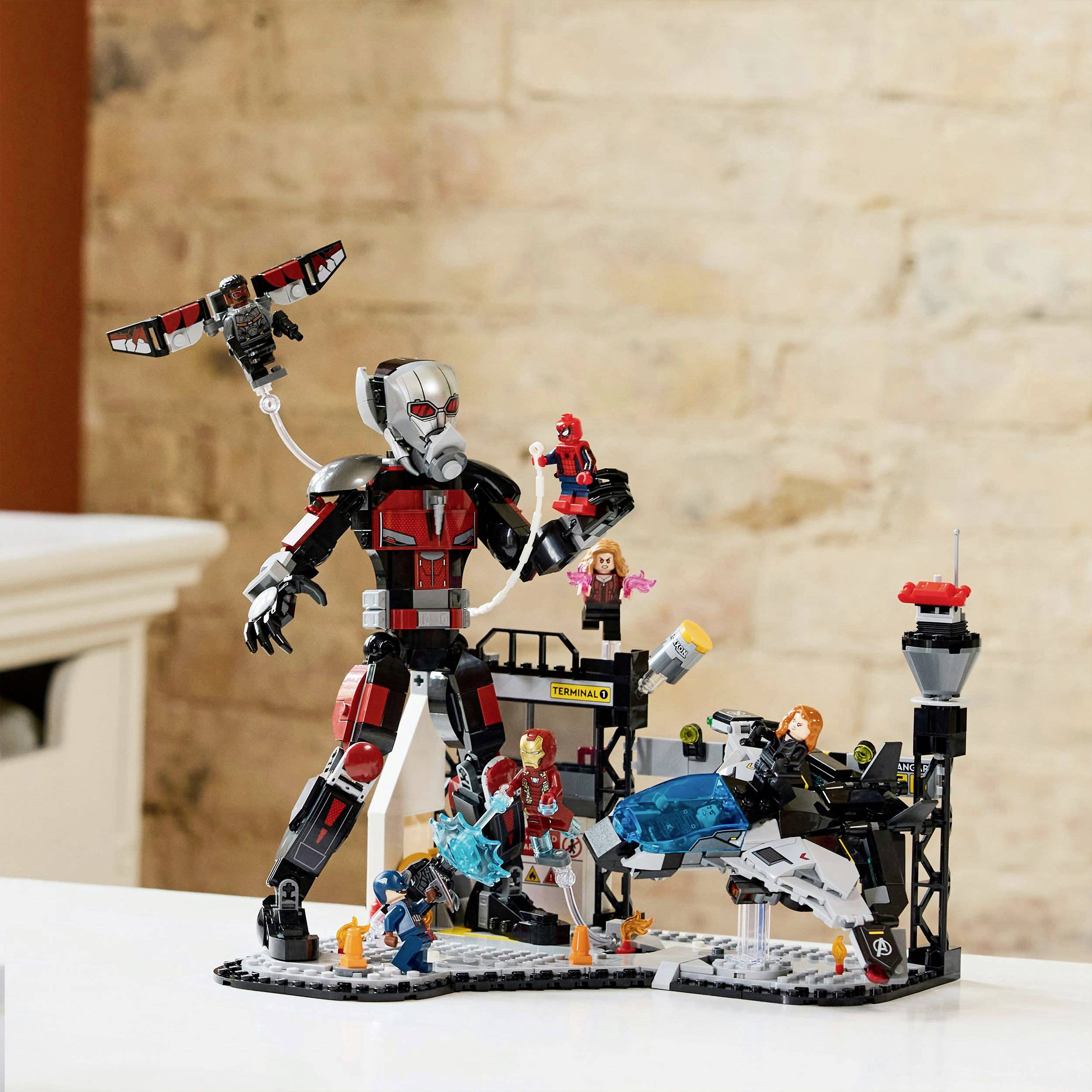 Budowla z klocków LEGO przedstawiająca scenę superbohaterów z robotami i postaciami na stole na tle ścian z cegły.