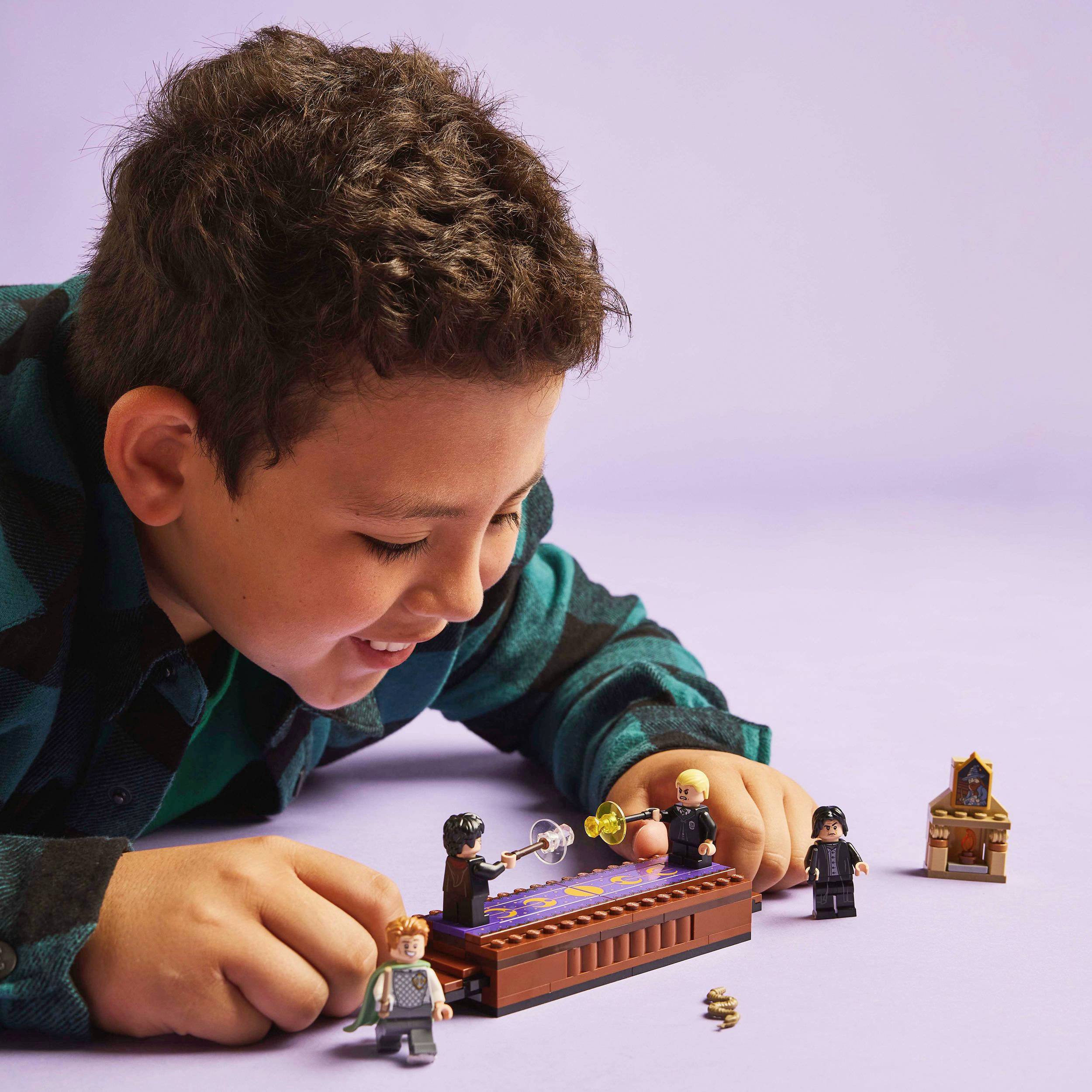 Uśmiechnięty chłopiec bawi się figurkami i klockami Lego na stole, otoczony fioletowym tłem.